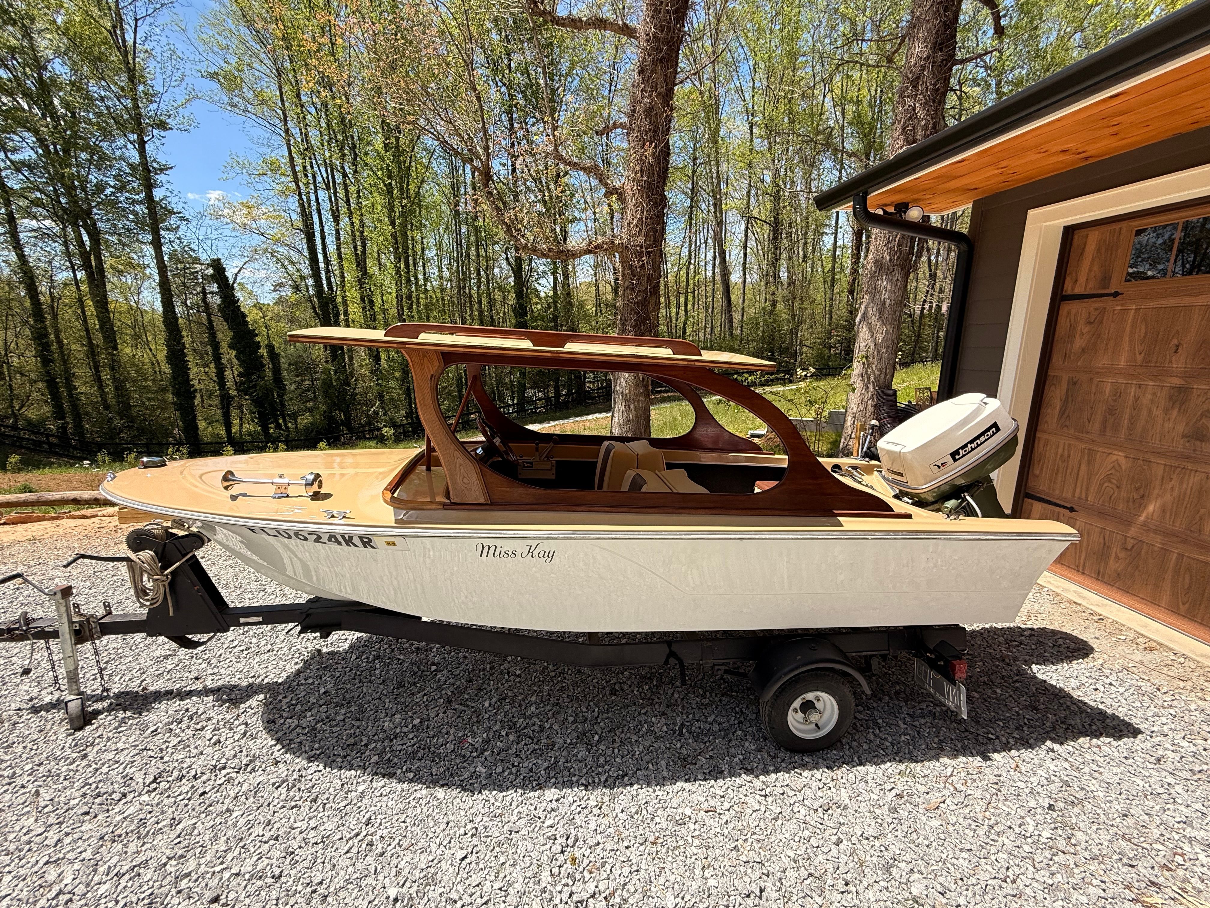 A vintage boat with wooden trim sits on a trailer next to a building.