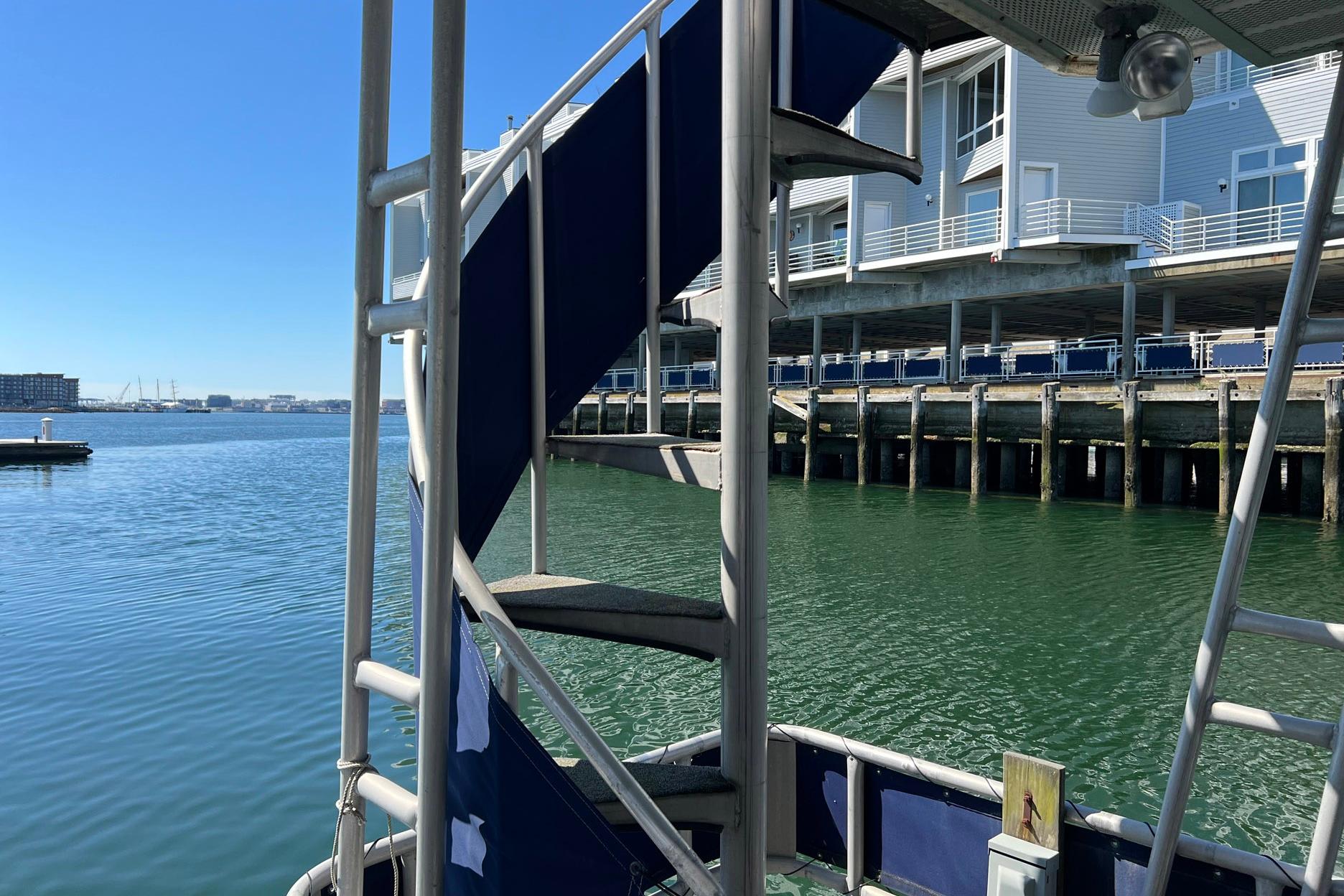 Spiral staircase on 1993 Sumerset houseboat docked by waterfront buildings.
