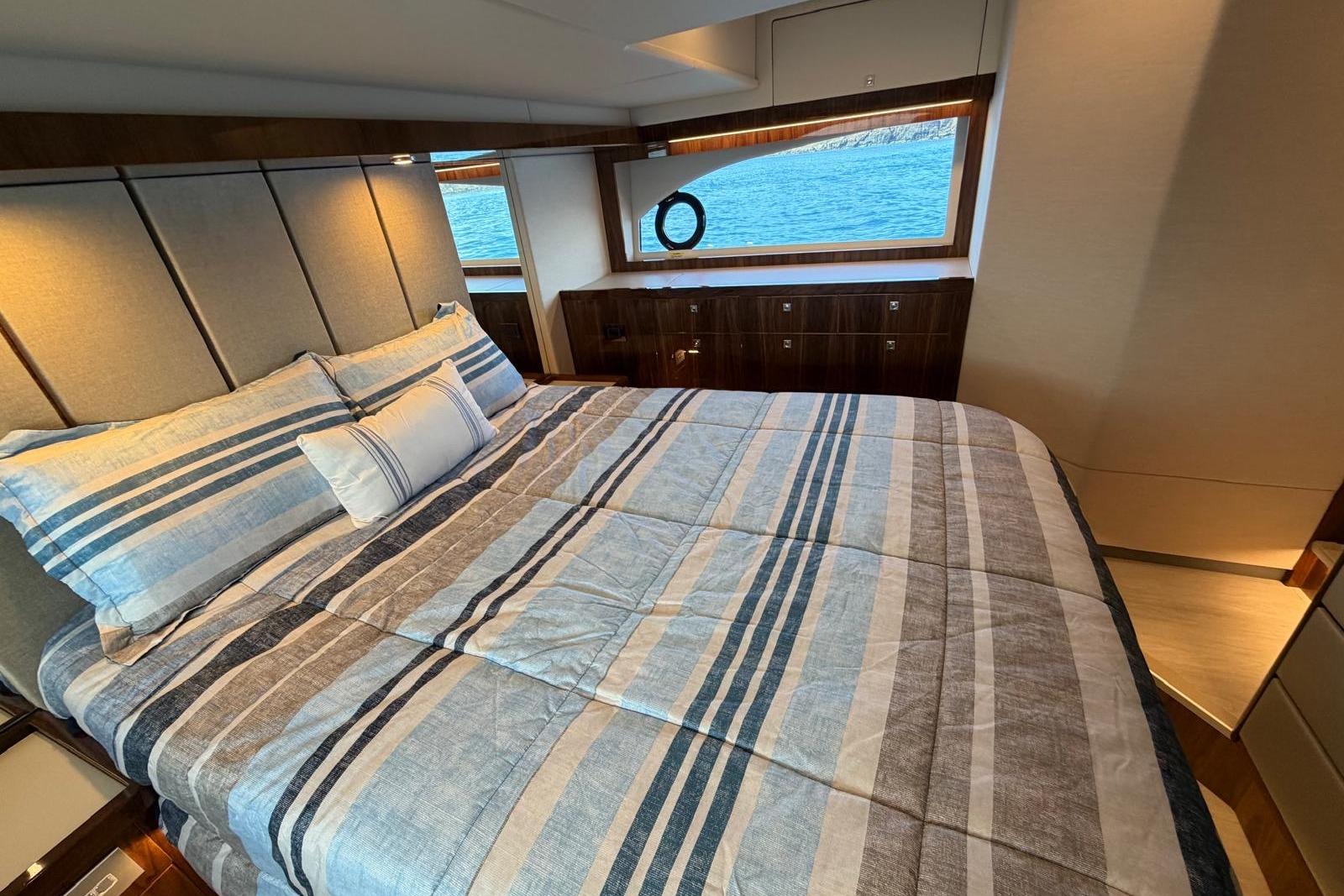 Luxurious bedroom interior of 2026 Riviera 505 SUV yacht with striped bedding and ocean view.