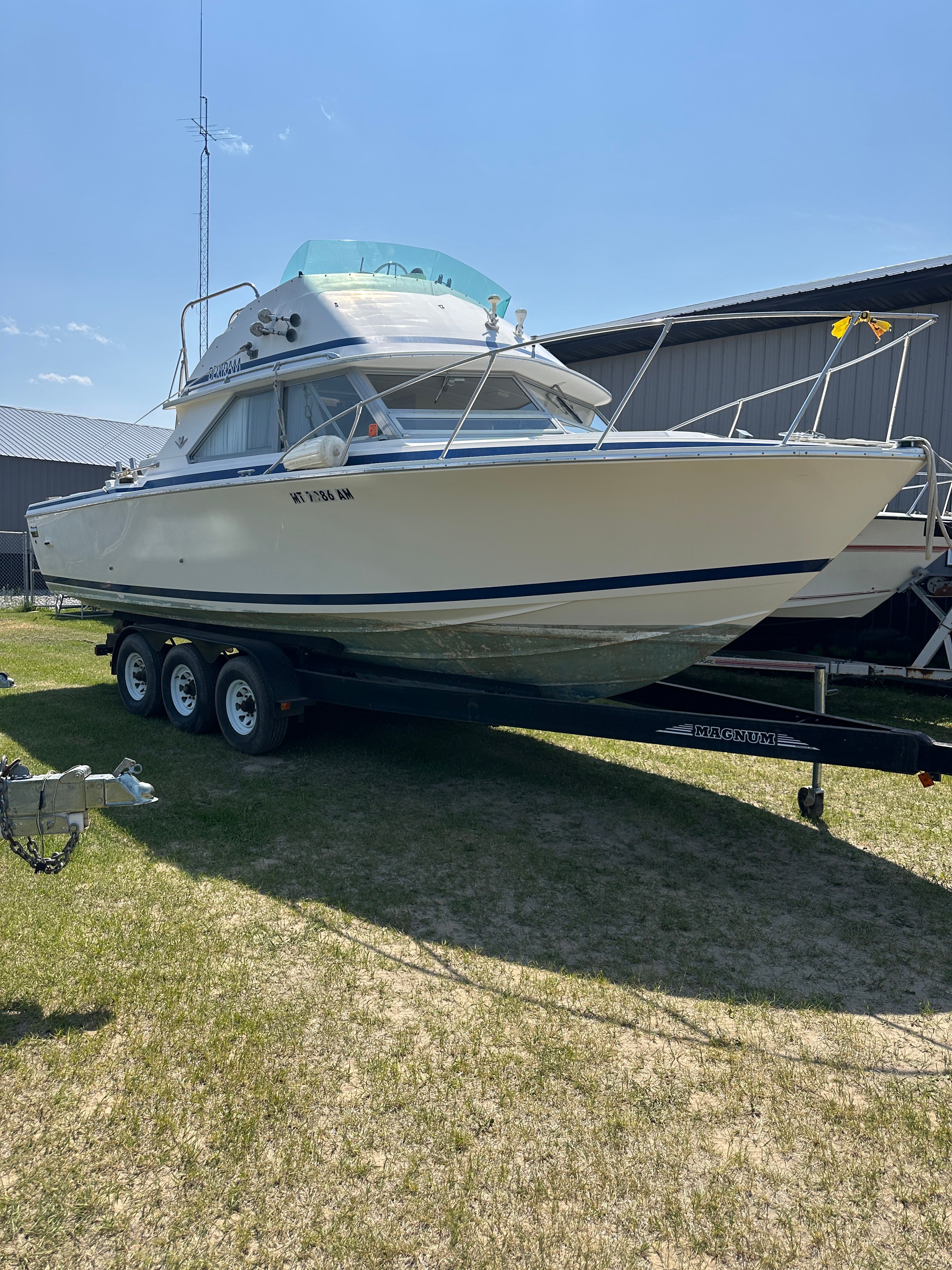 A 1983 Bertram Flybridge Cruiser is on a trailer outdoors.