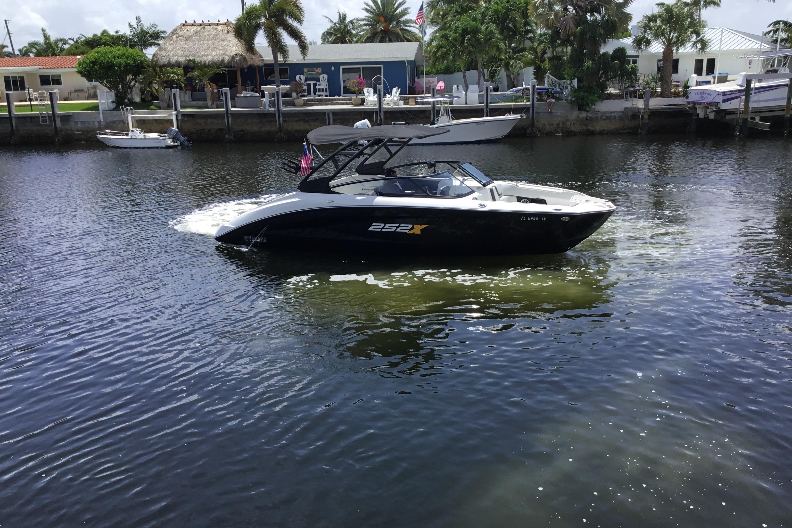 2023 Yamaha Boats 252XE cruising on a sunny waterfront with palm trees.