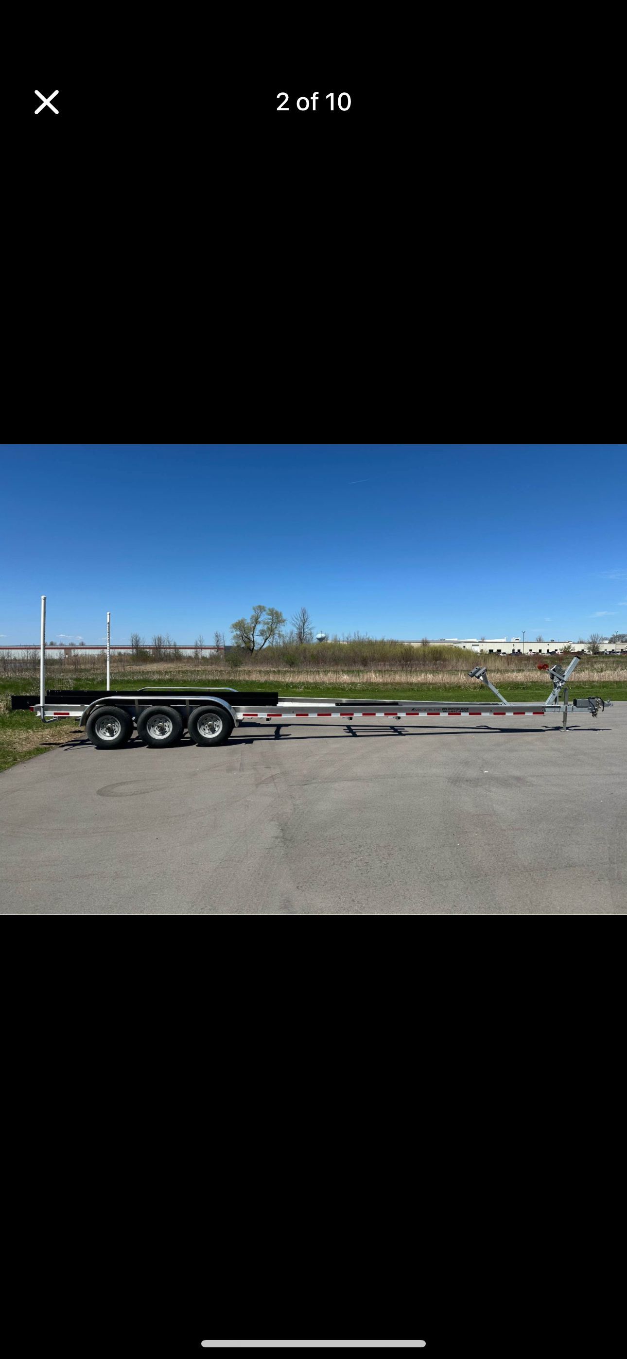 A triple-axle boat trailer is parked on a lot under a clear blue sky.