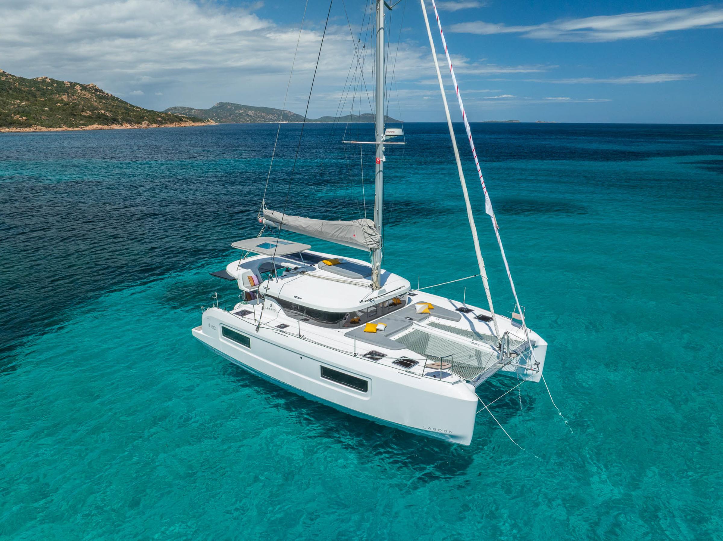 2025 Lagoon 38 catamaran sailing in clear turquoise waters, under a partly cloudy sky.
