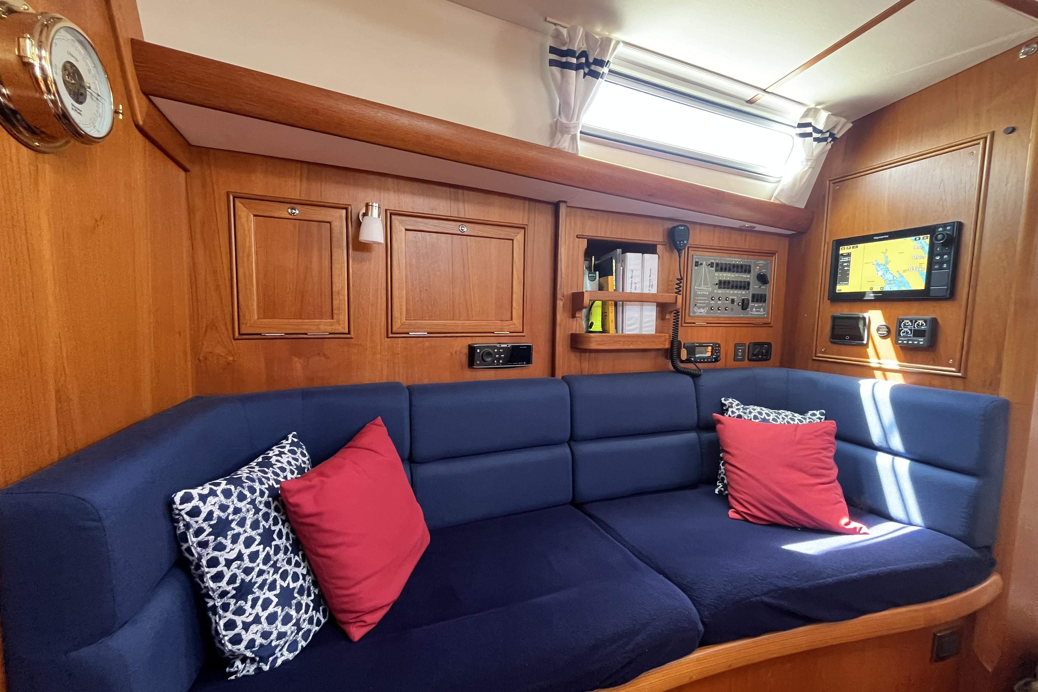 Interior of 2017 Rustler 37 yacht with blue seating, red pillows, and navigation equipment.
