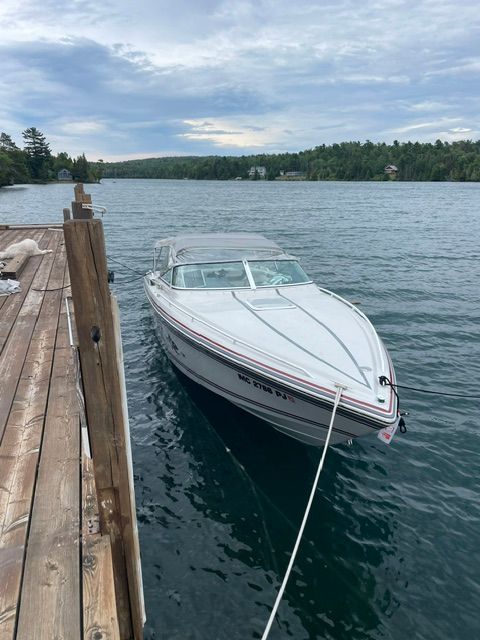 A white motorboat docked at a wooden pier, floating on a calm lake.
