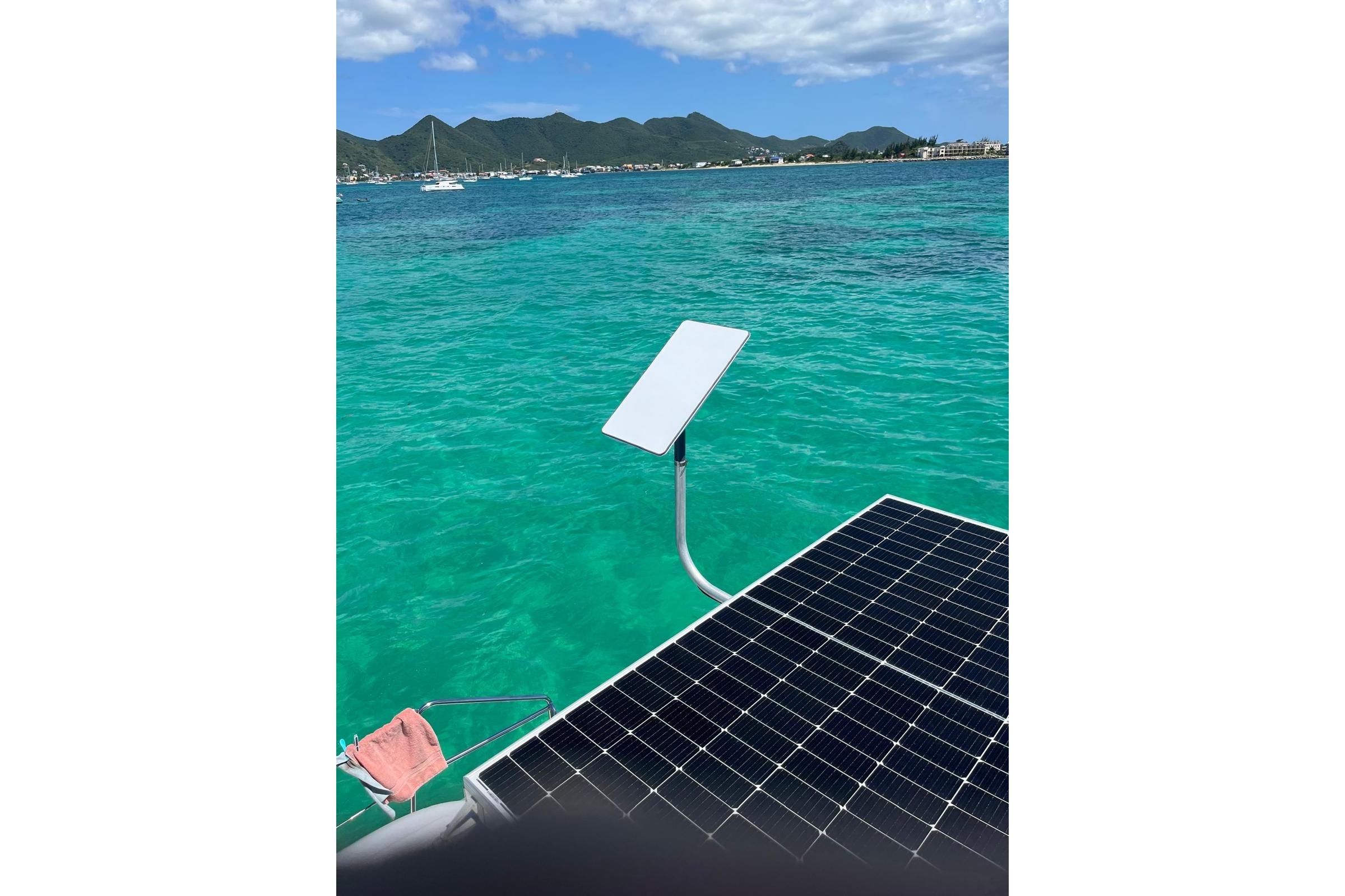 Lagoon 400 catamaran with solar panel and Starlink, turquoise sea, mountainous coastline.