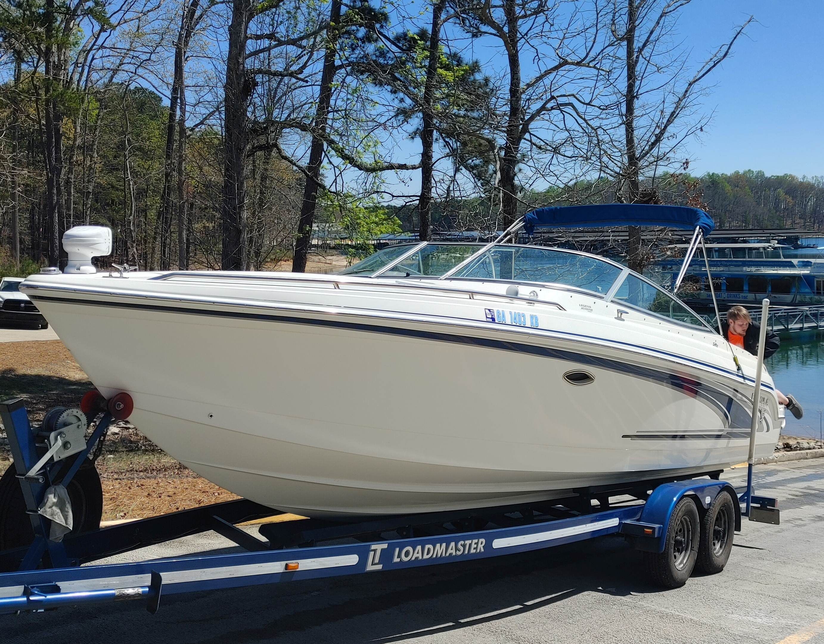 A white motorboat on a trailer, featuring a blue sunshade, parked on land.