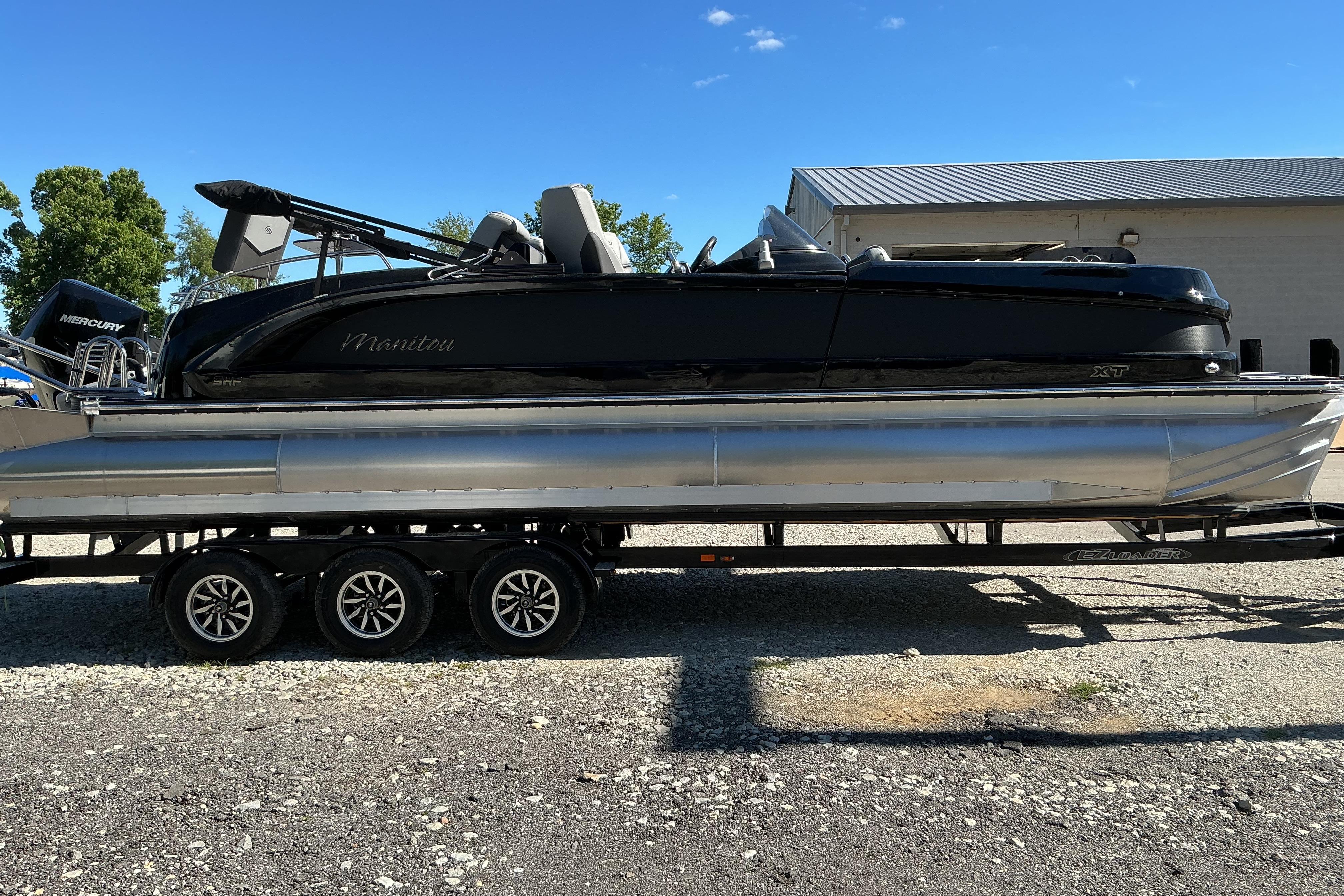 2024 Manitou 25 X-Plode XT SRS pontoon boat on trailer, parked outdoors.