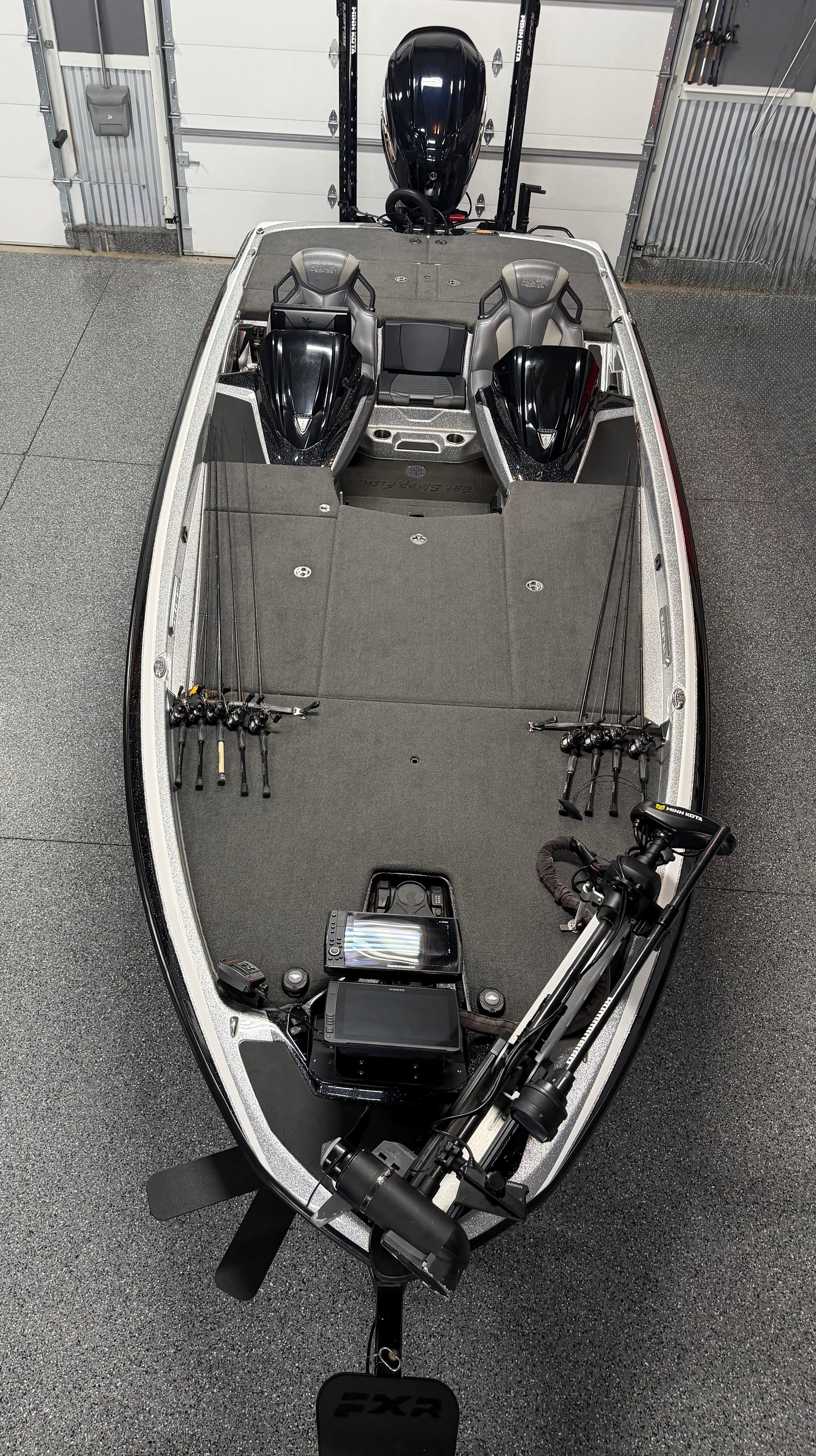 A modern fishing boat with a gray deck and multiple fishing rods, parked in a garage.