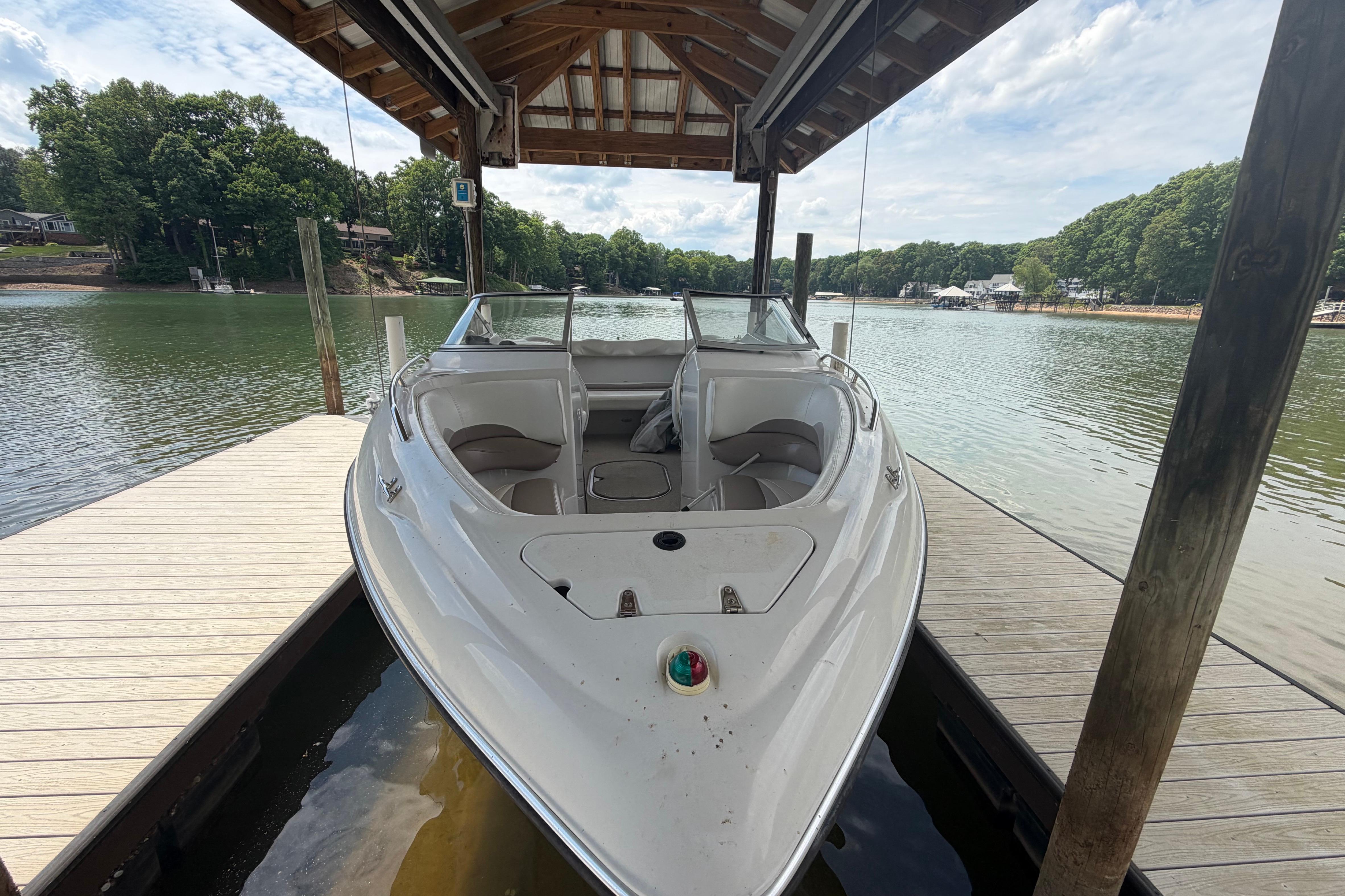 1998 Four Winns 220 Horizon boat docked under a wooden canopy on a serene lake.