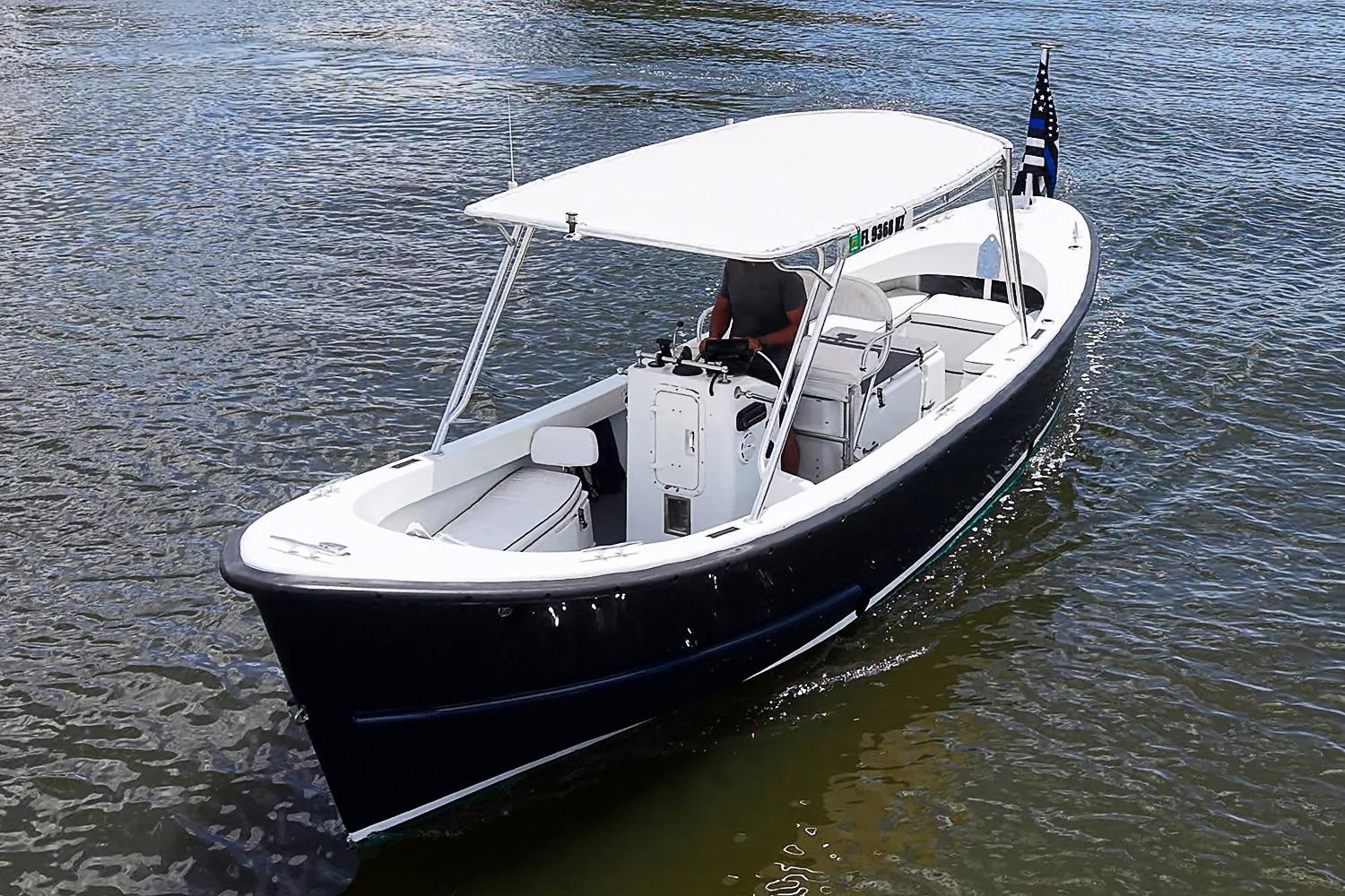 Custom 1969 boat with canopy cruising on water, featuring sleek design and American flag.
