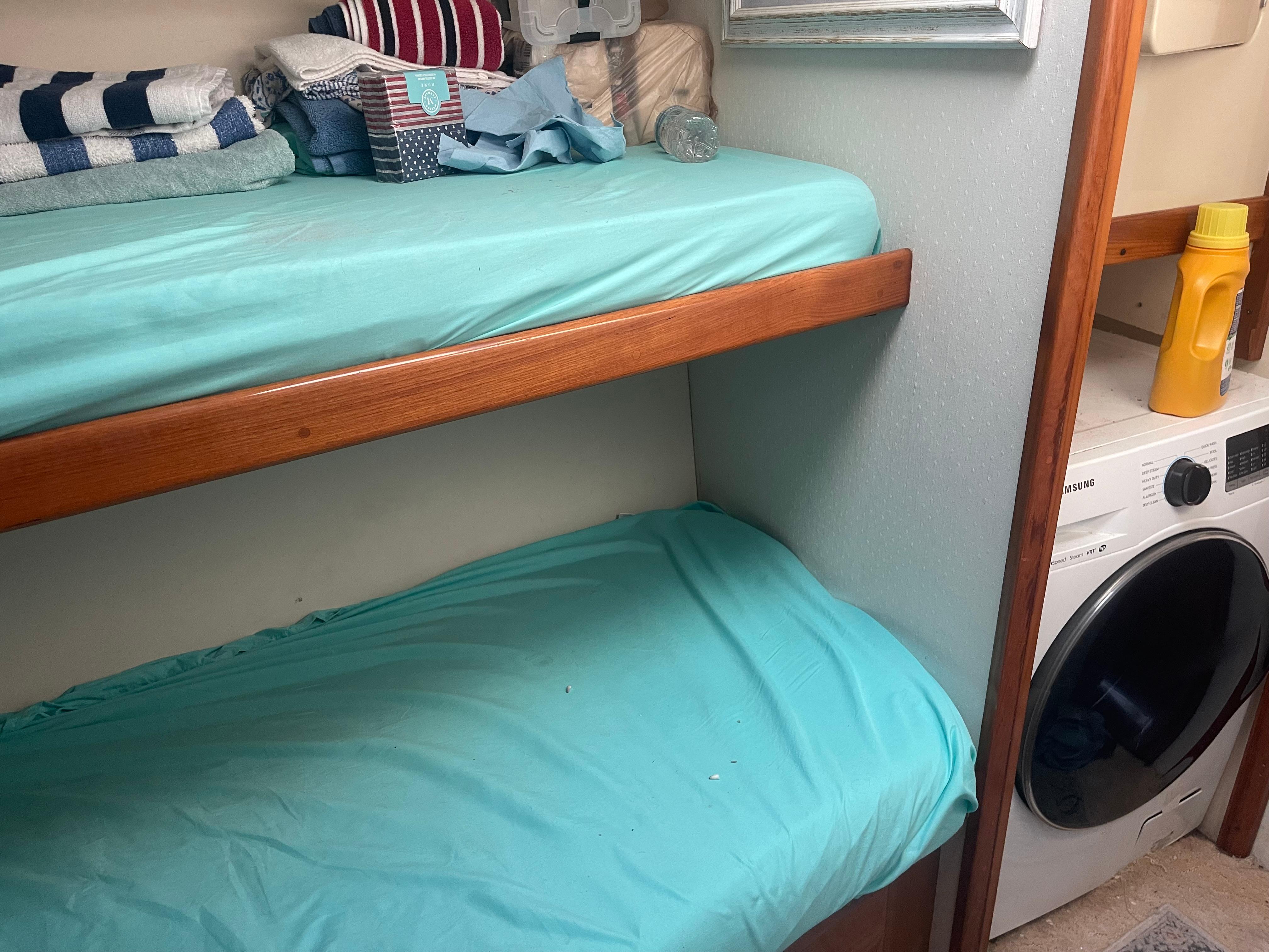 Bunk beds with teal sheets in a 1999 Viking 58 EB yacht cabin, adjacent to a washing machine.
