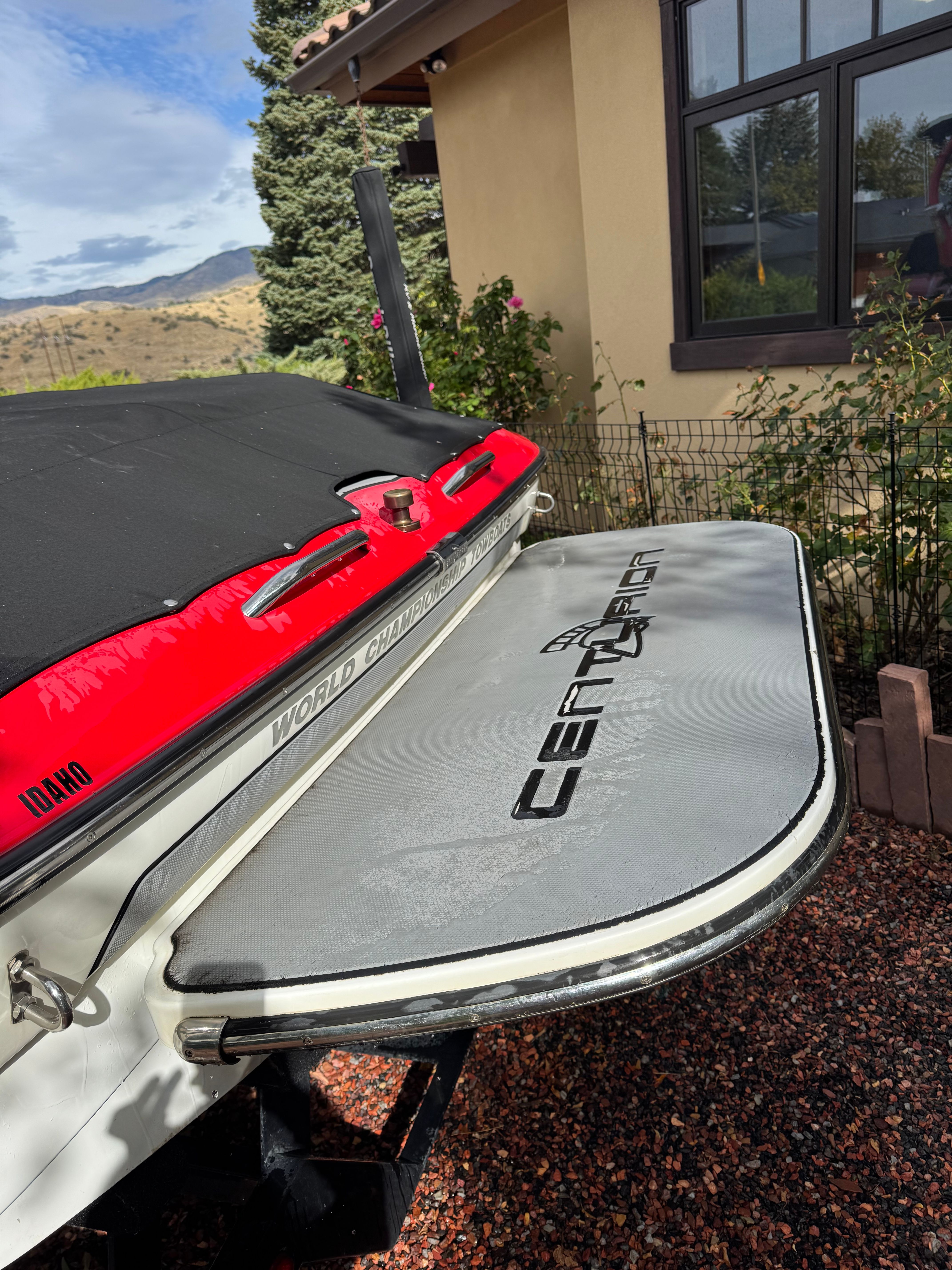 A 2013 Centurion Enzo SV211 with a red and gray stern, parked beside a house.