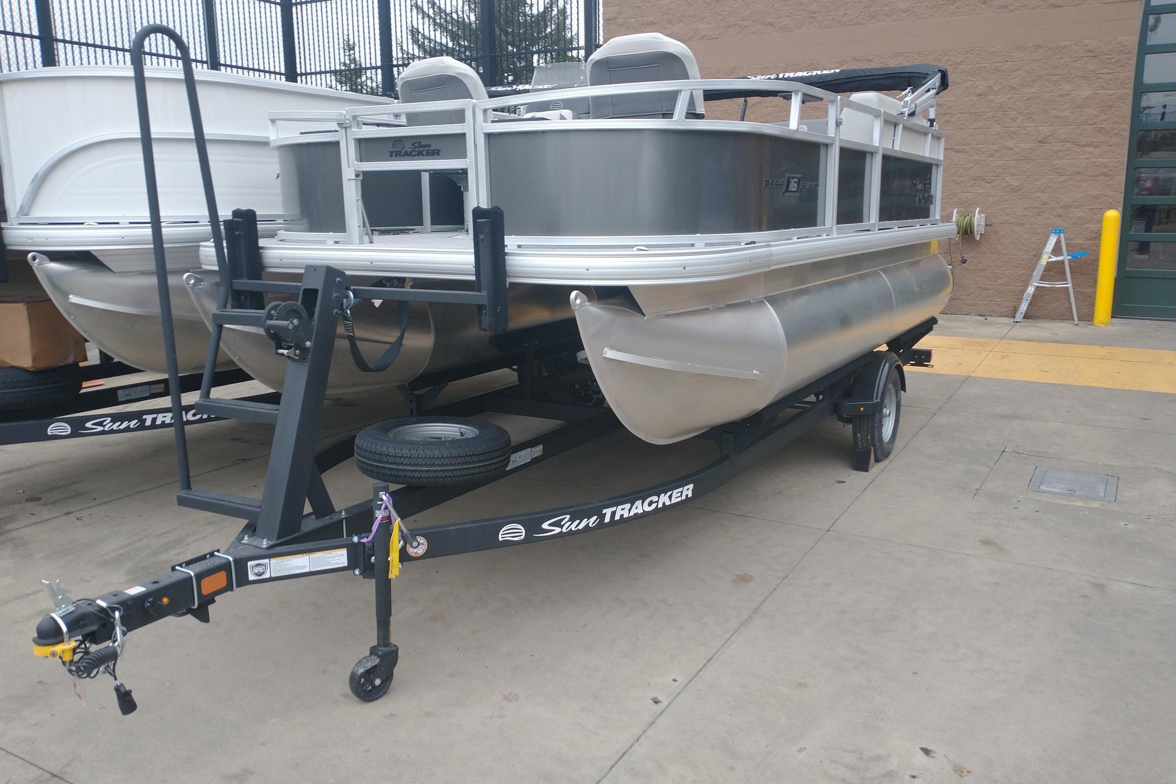 2026 Sun Tracker Bass Buggy 16 XL Select pontoon boat on trailer, parked outdoors.