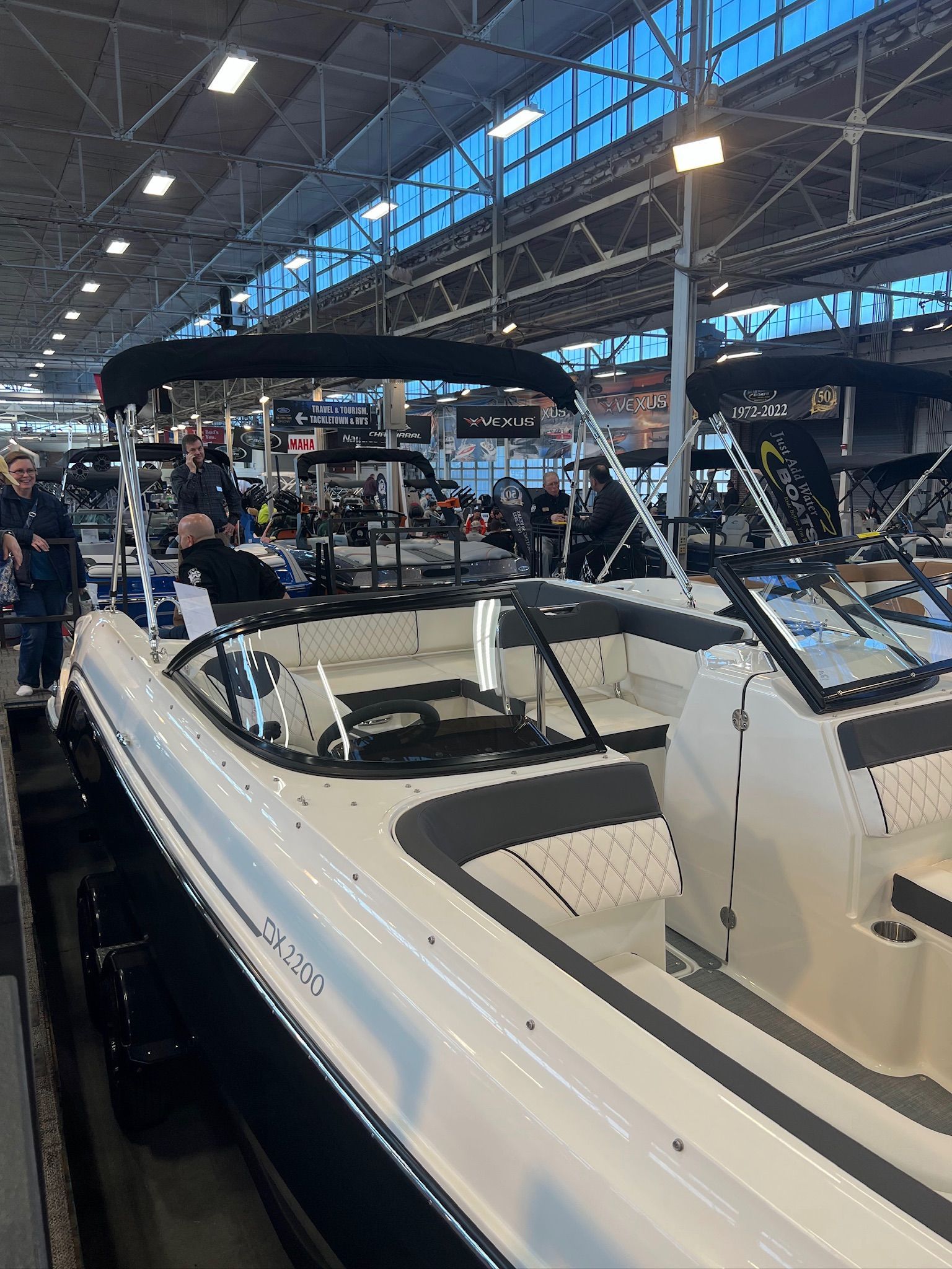 2022 Bayliner DX 2250 boat displayed at an indoor exhibition with people observing.