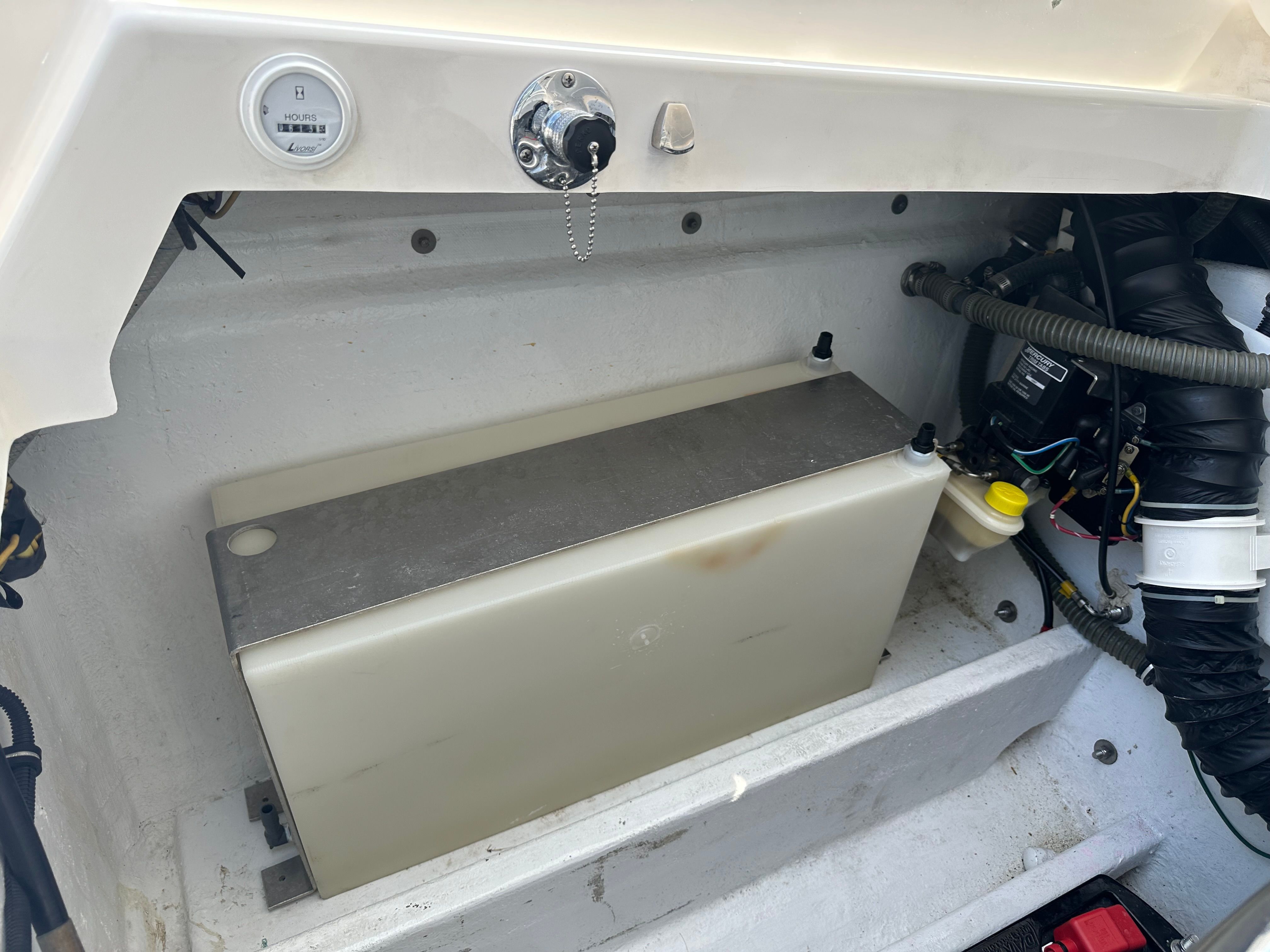An open boat engine compartment with a rectangular tank and hoses.