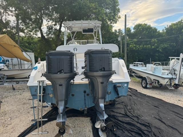 2007 Cobia 270 boat with dual outboard motors, parked on gravel near trees and other boats.