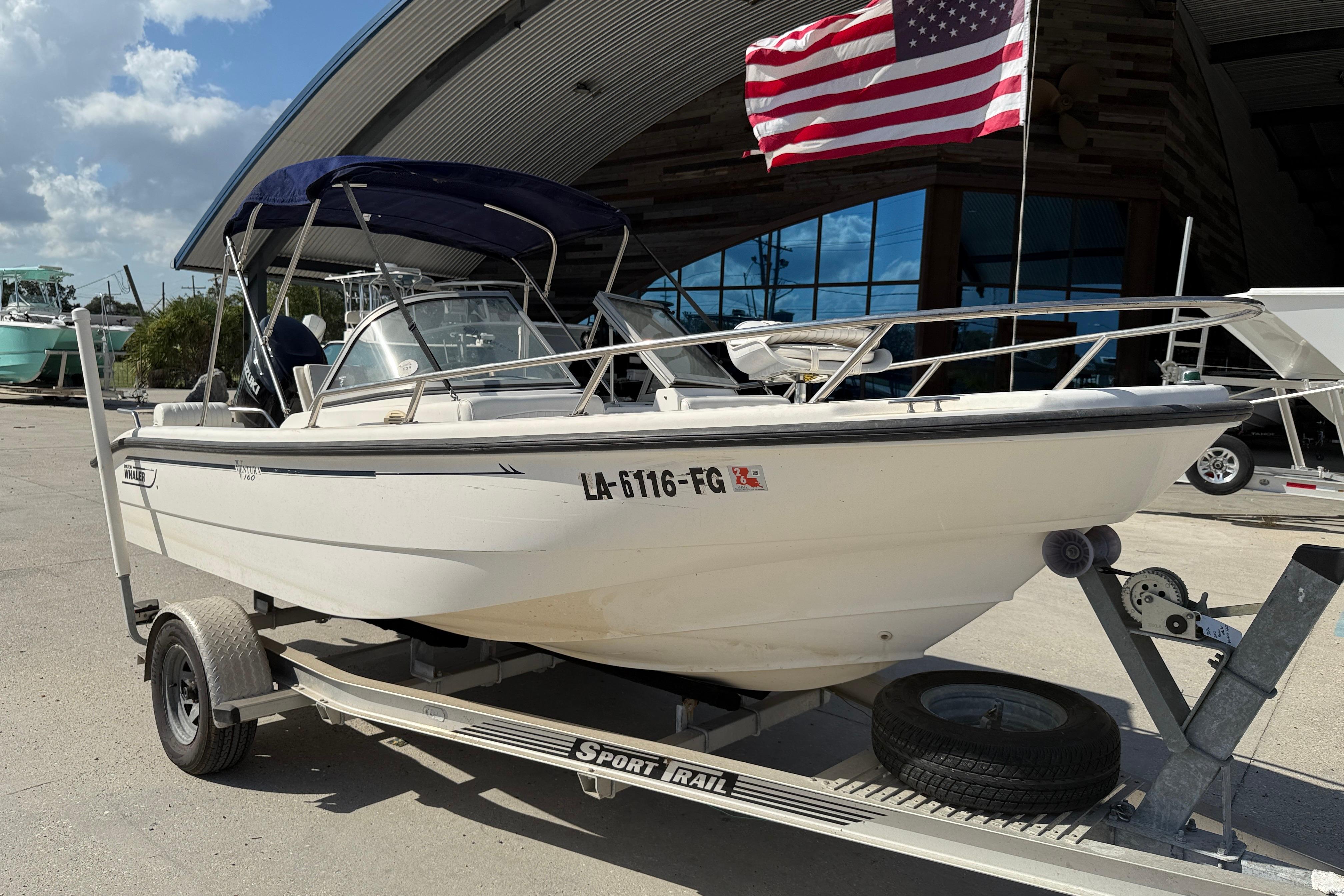 2002 Boston Whaler Ventura 160 boat on trailer with American flag, parked outdoors.