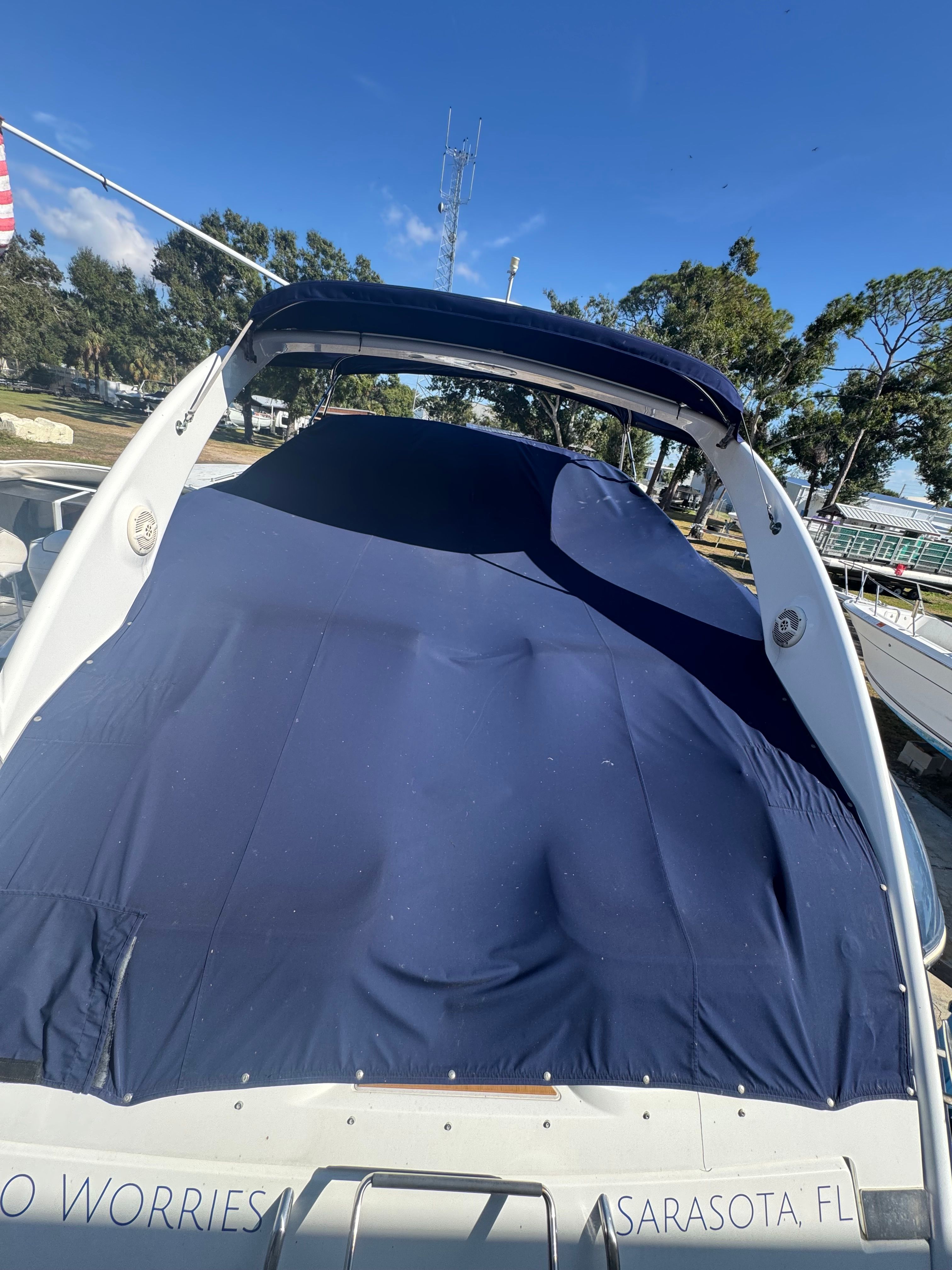 A 2003 Cobalt 360 boat with a blue cover, parked on land under a blue sky.