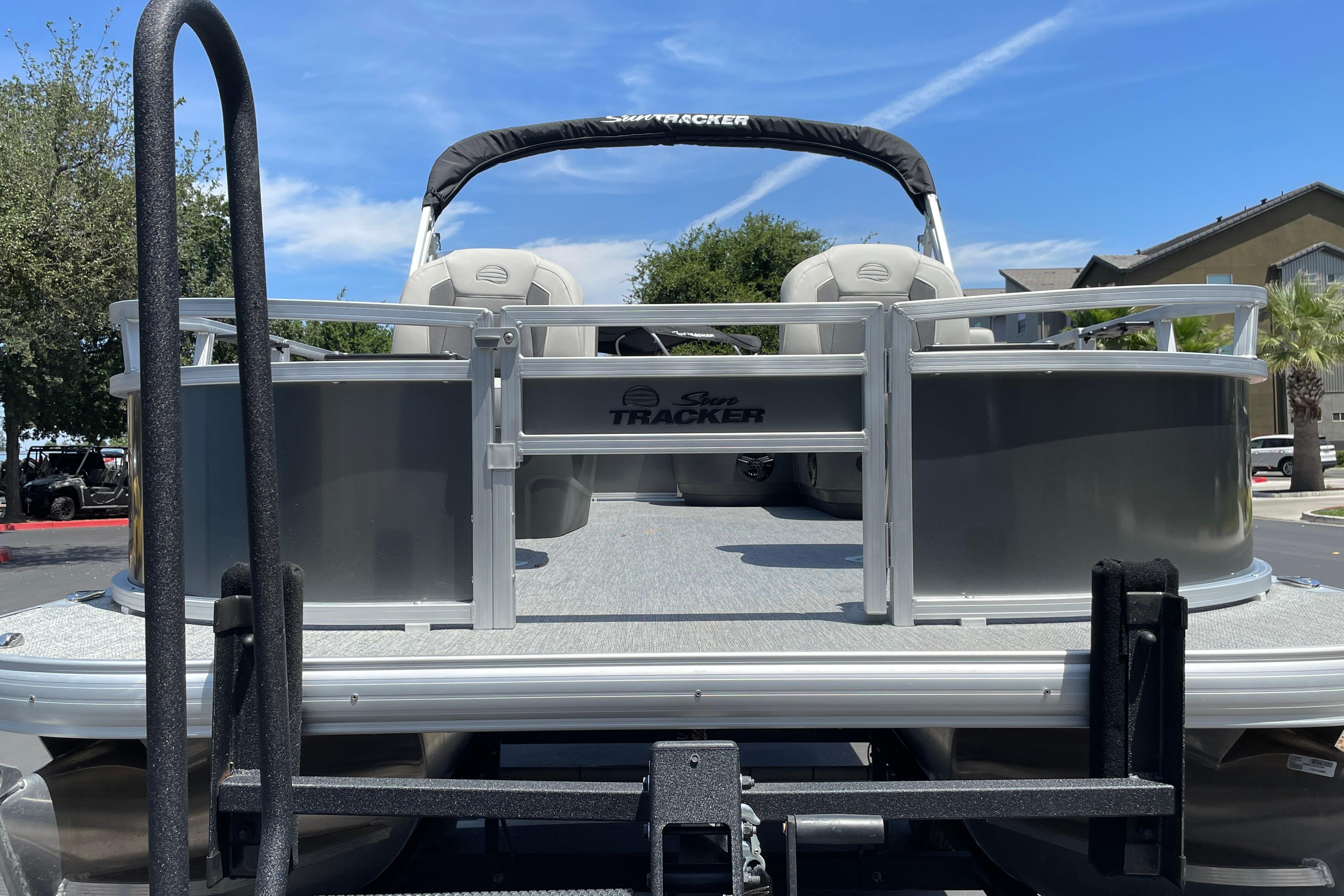 2026 Sun Tracker Bass Buggy 16 XL Select pontoon boat on trailer, parked outdoors.