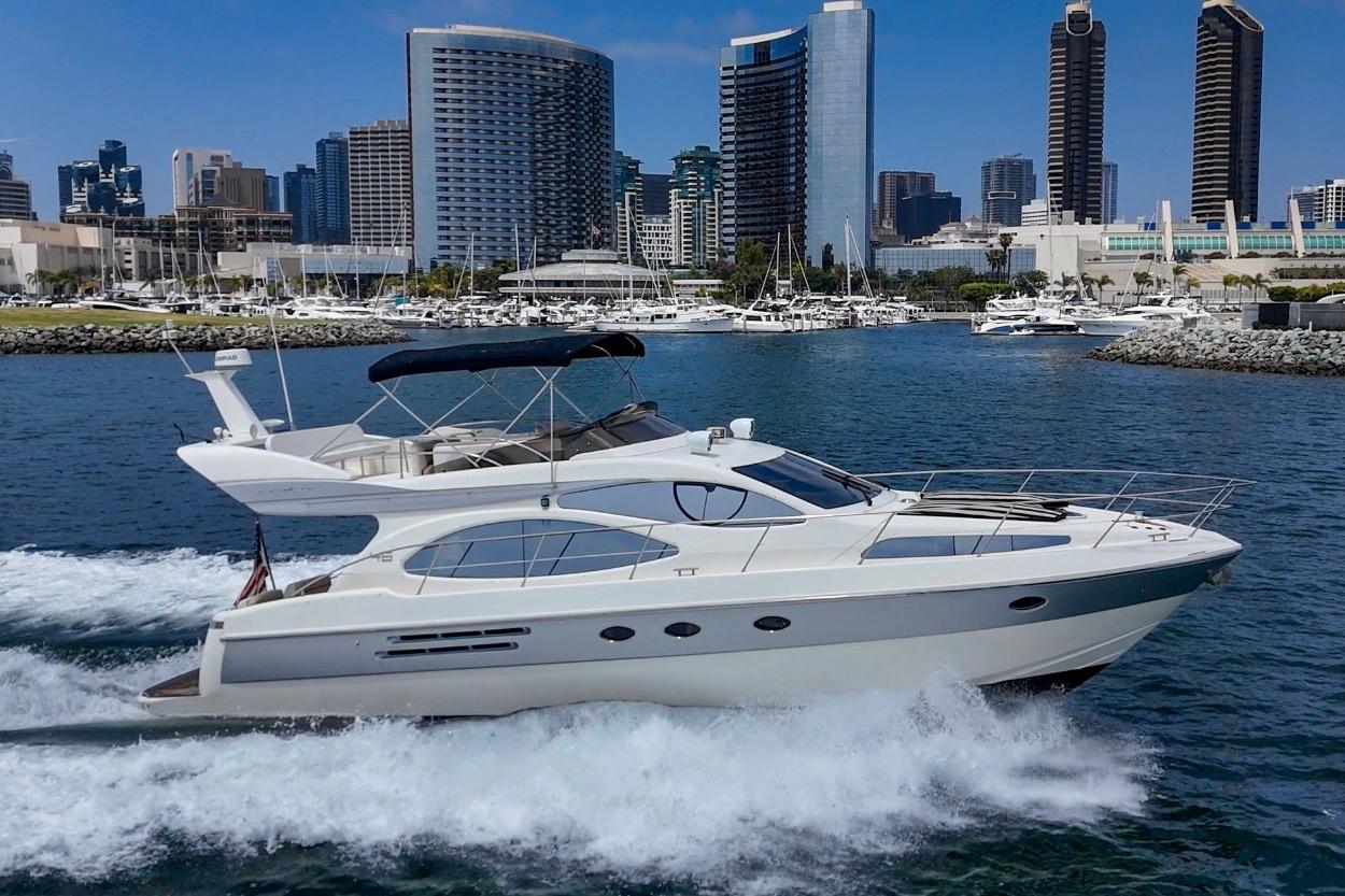 2004 Azimut 46 yacht cruising in a marina with city skyline backdrop.