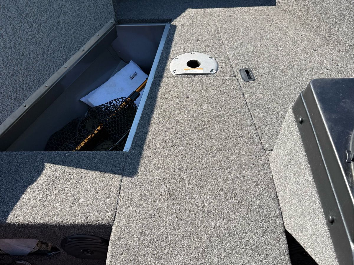 The image shows a boat interior with gray carpeting and an open storage compartment.