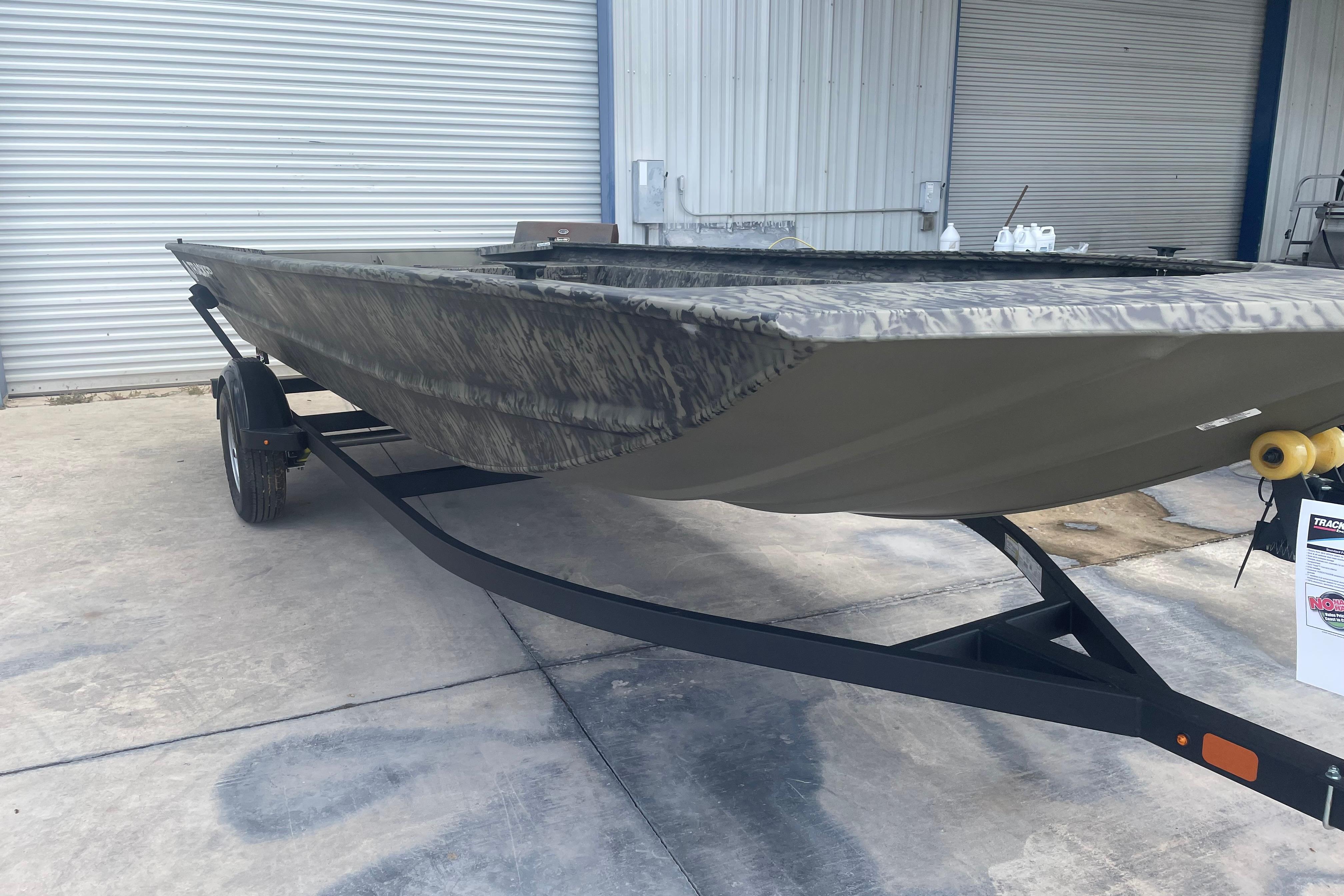 2026 Tracker Grizzly 1860 Utility boat on trailer, parked outside a garage.