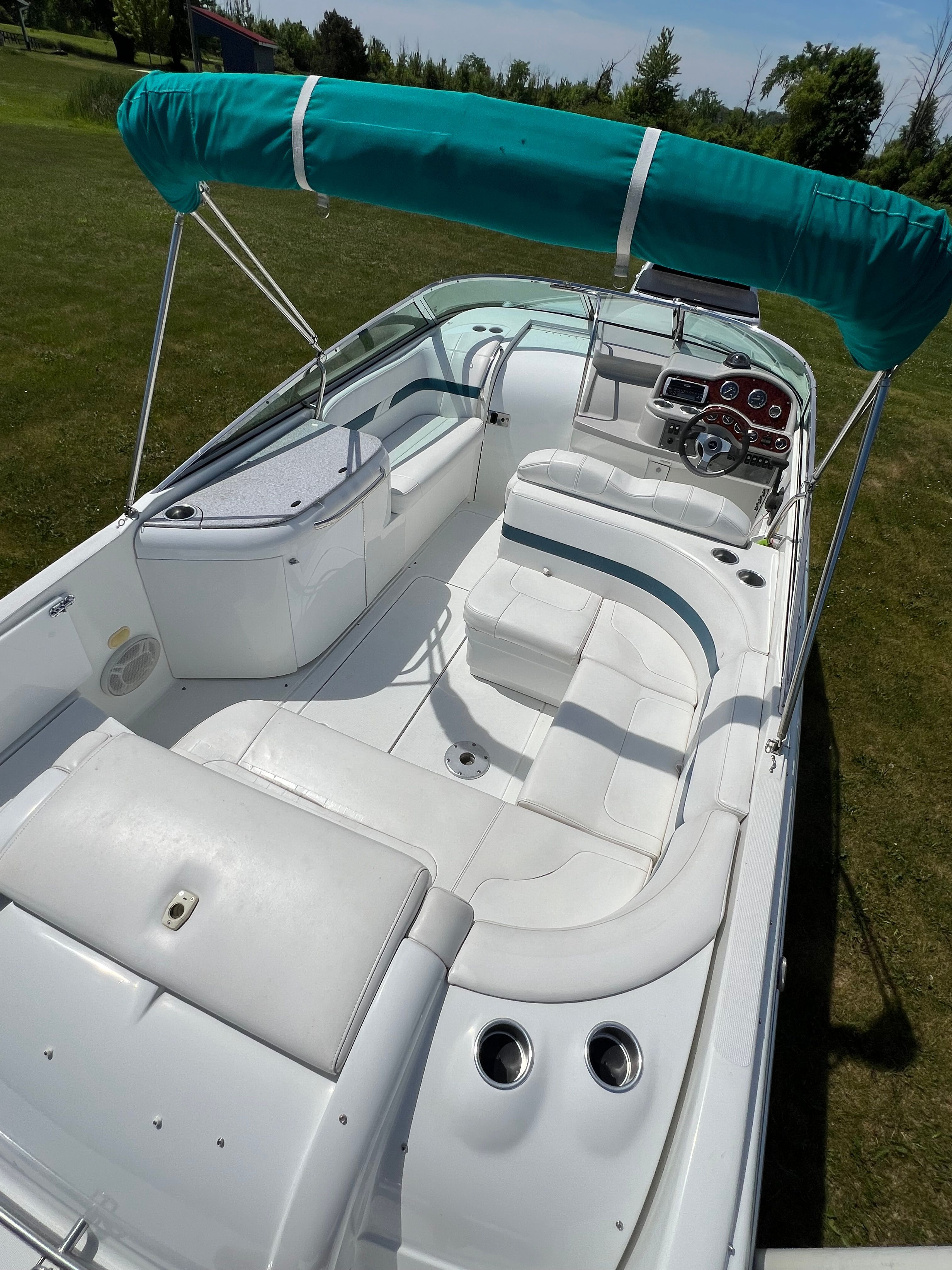 The image shows a white boat with a turquoise sunshade, luxurious seating, and a modern dashboard.