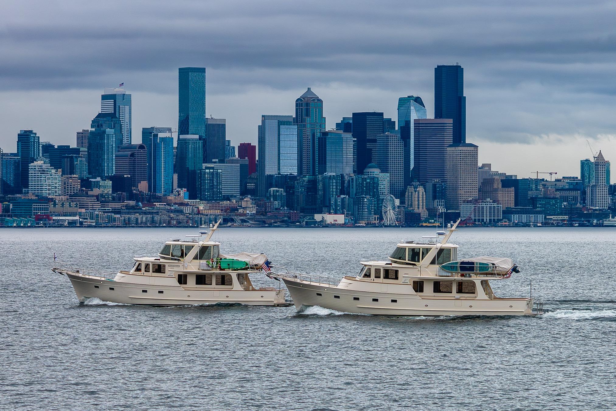 Two Fleming 55 Pilothouse yachts cruising near a city skyline under cloudy skies.