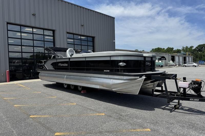 2026 Manitou Encore 25 SL SHP pontoon boat parked outside a large garage.