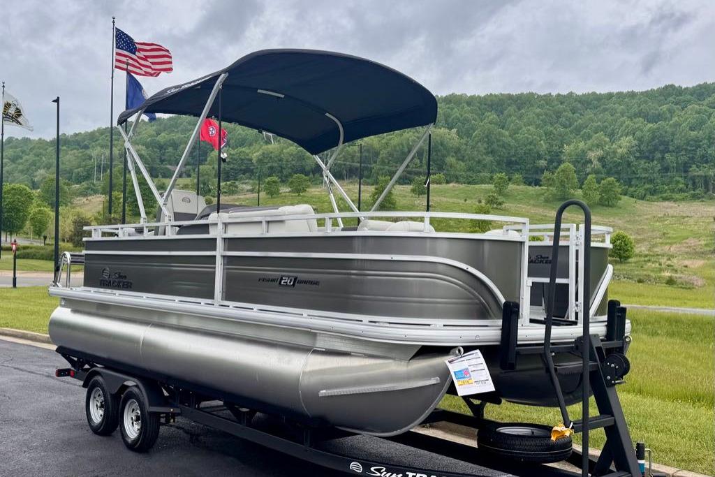 2026 Sun Tracker Fishin' Barge 20 DLX pontoon boat on trailer, flags in background.