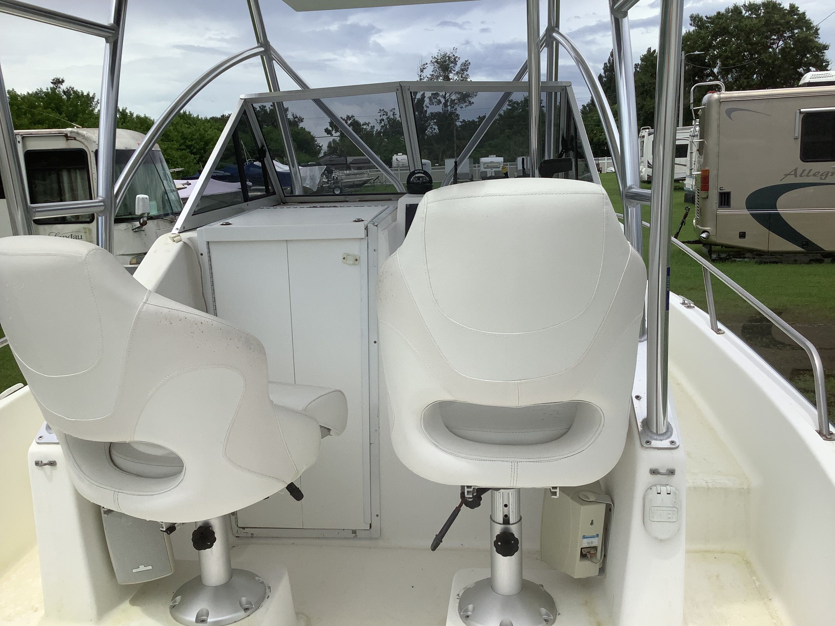 Two white seats on a boat with a steering console and railing.