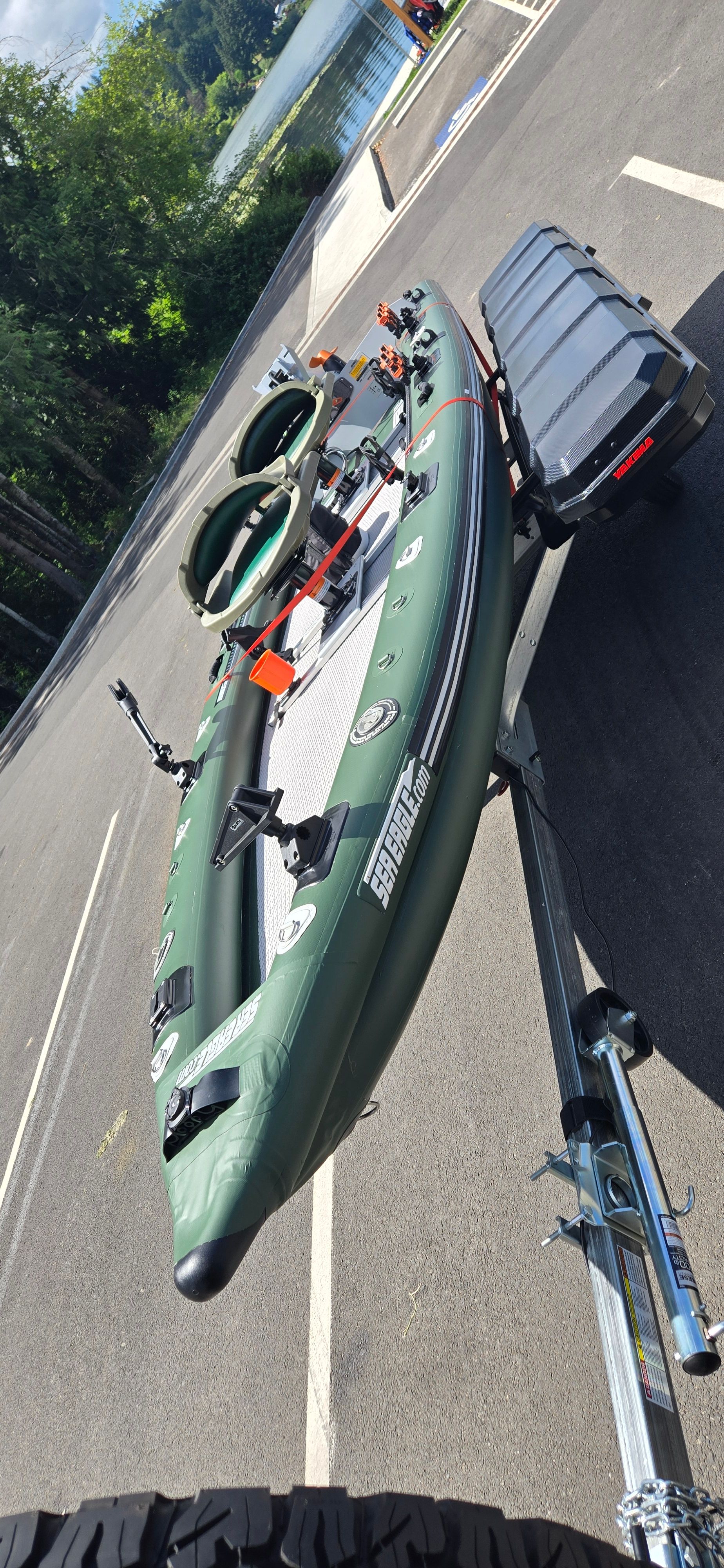 A green inflatable boat on a trailer, ready for use by the water.