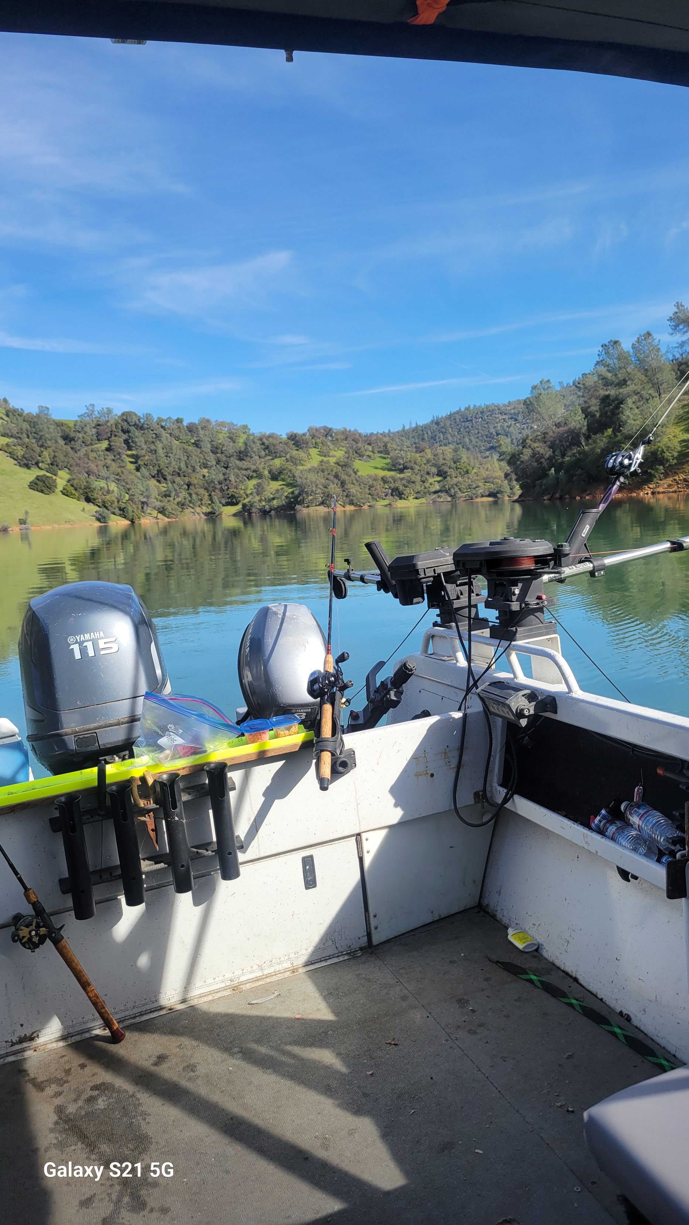 The image shows the stern of a boat with fishing rods and motors on a calm lake.