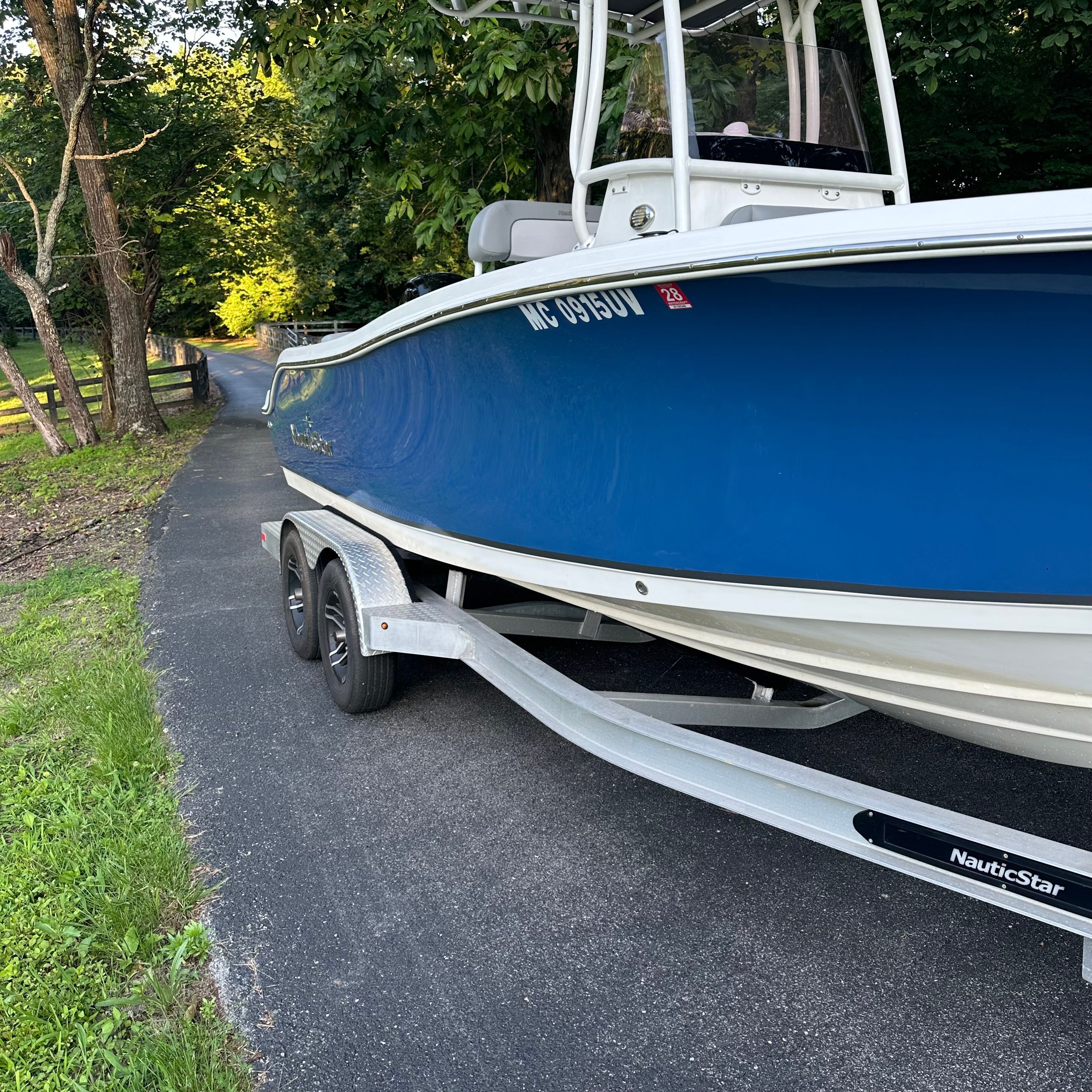 NauticStar 2102 Legacy 2022 on a trailer, surrounded by trees on a road.