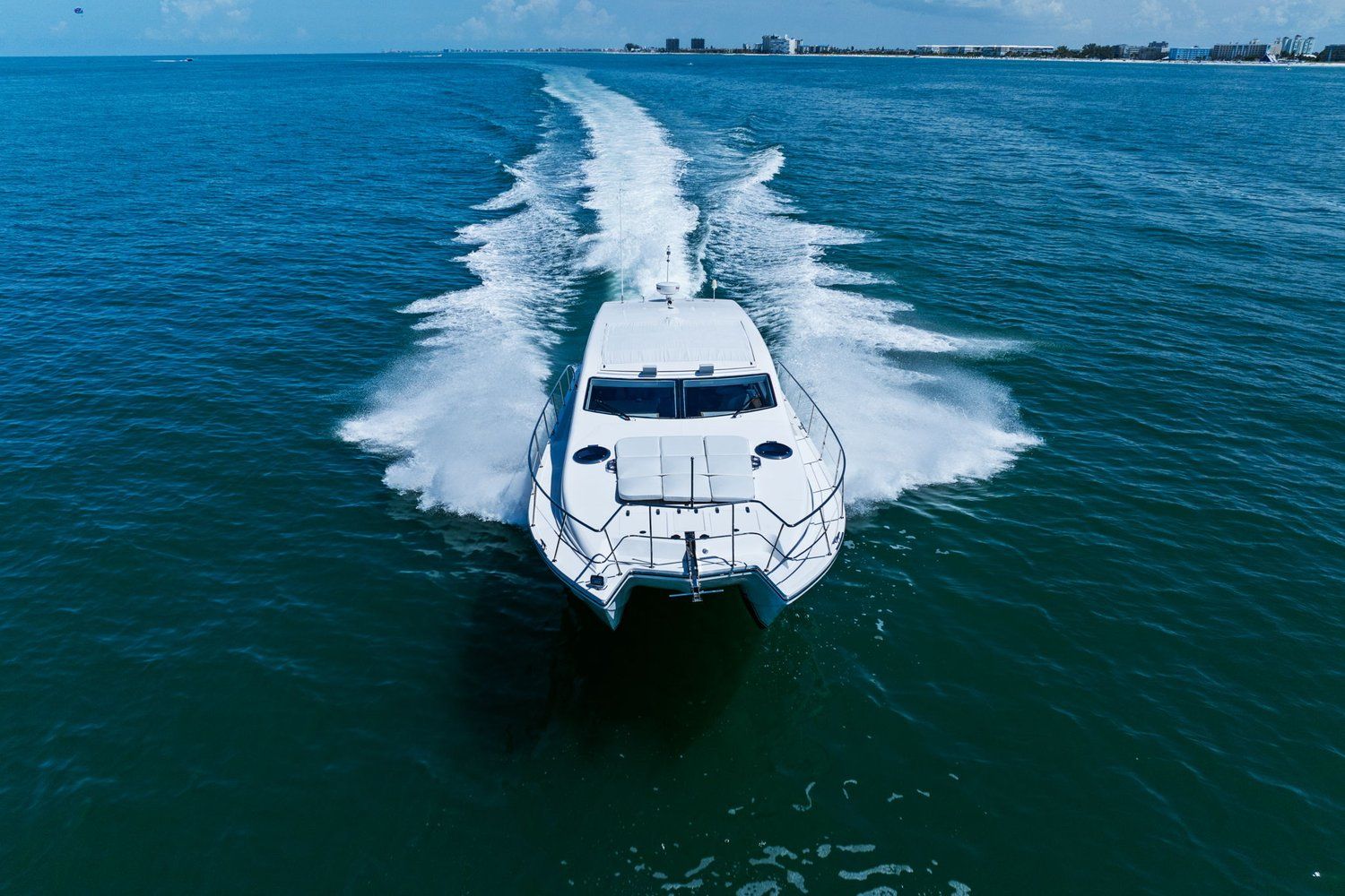 A white catamaran speeds across the blue sea, leaving a trail of spray.