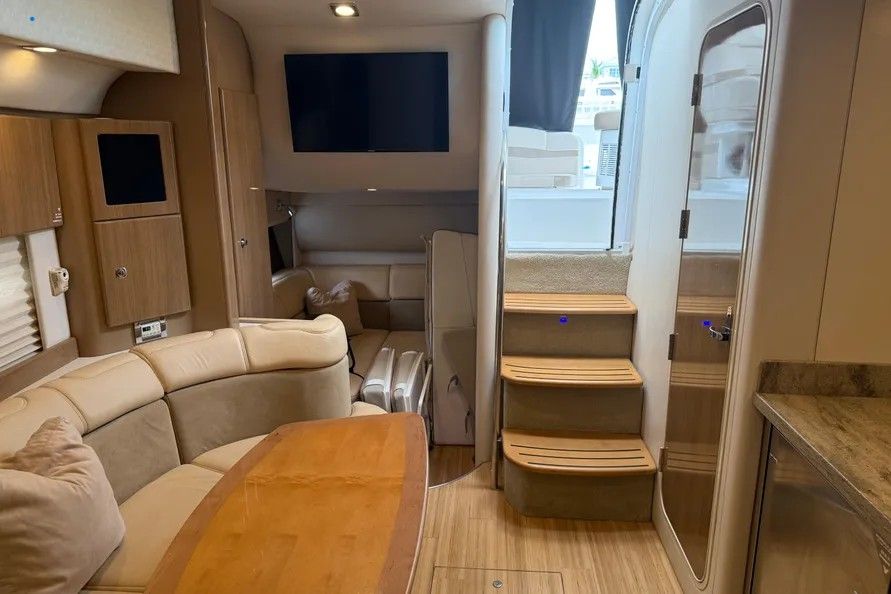 Interior of a luxury yacht with beige sofa, wooden table, and stairs to upper level.