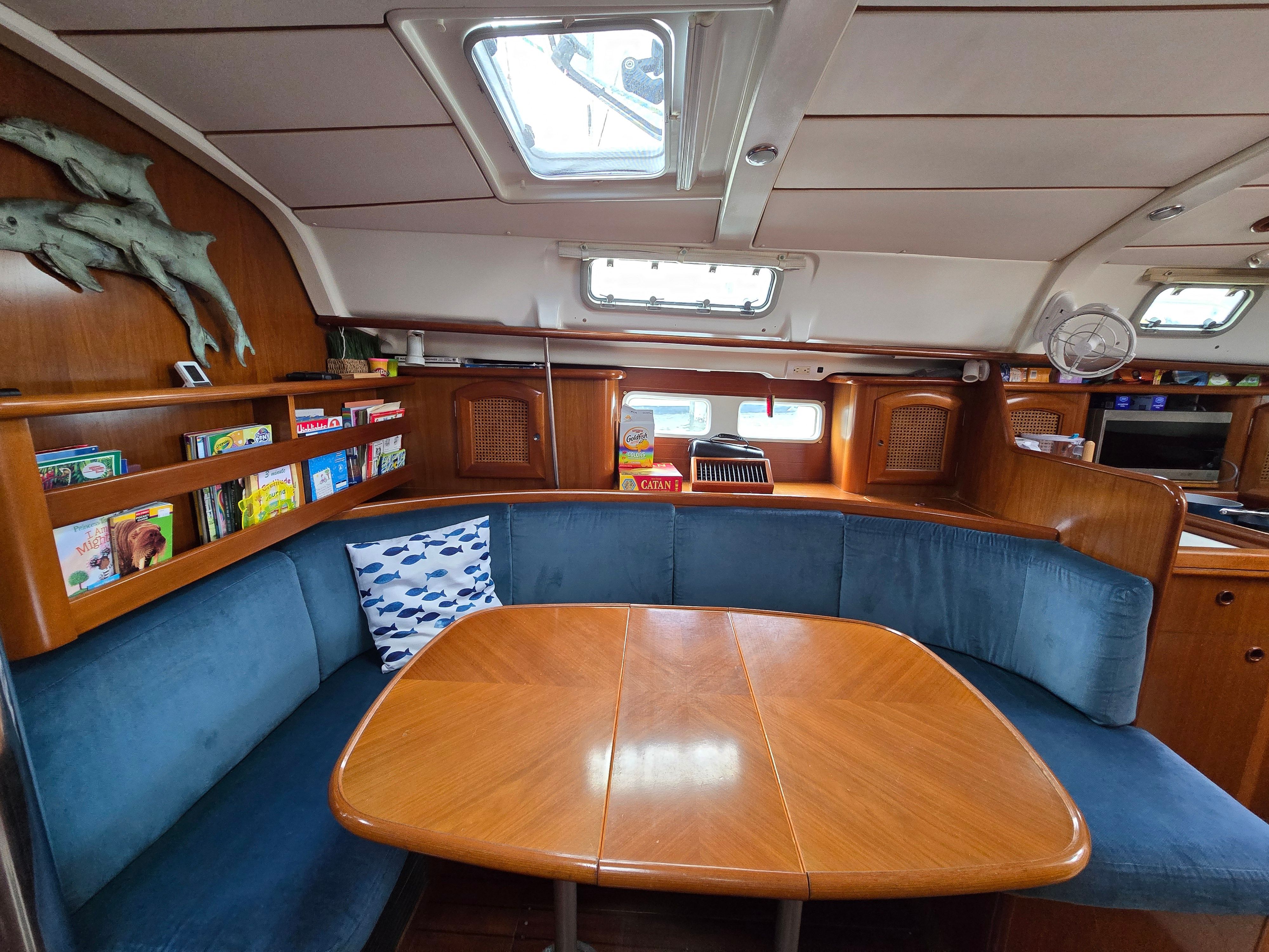 Interior of a 1998 Beneteau 411 with a wooden table and blue upholstered seating.