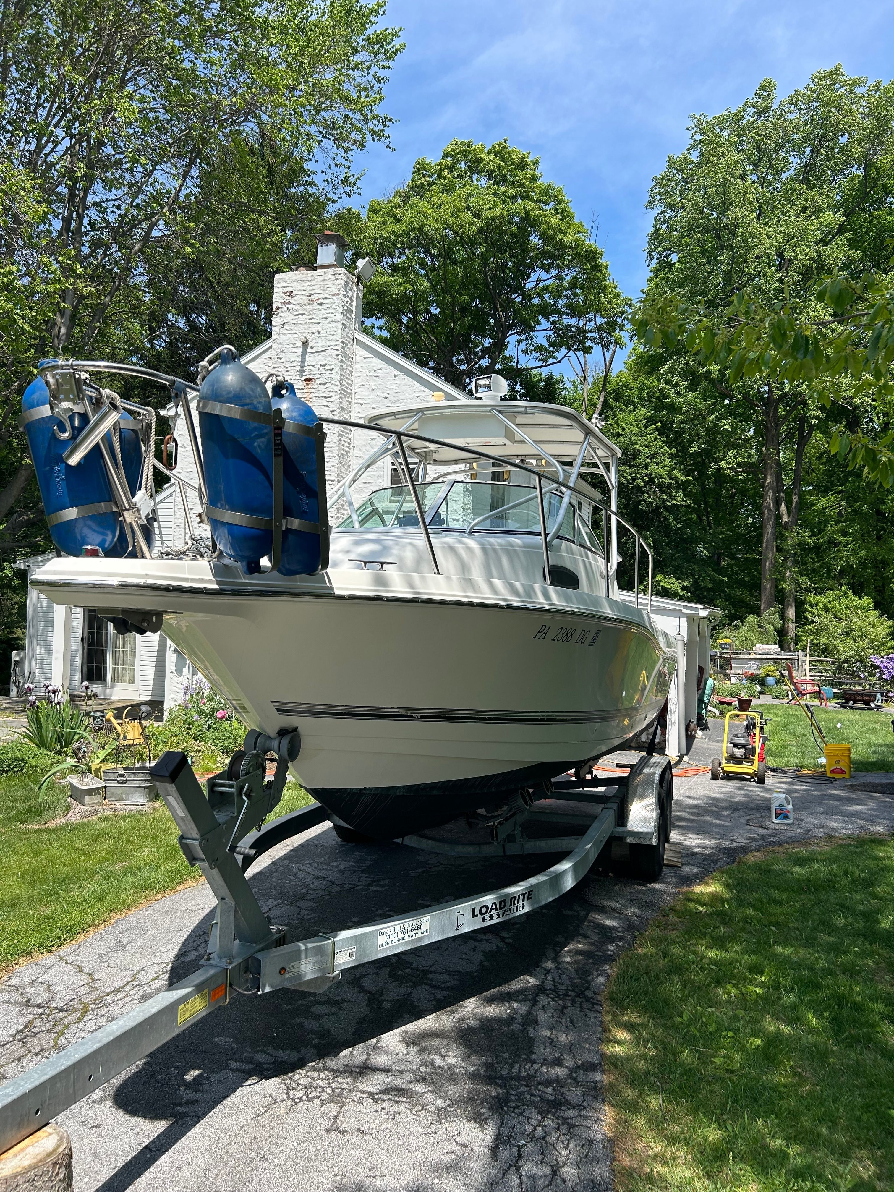 A 2002 Wellcraft 24 Walkaround boat on a trailer in a green garden setting.