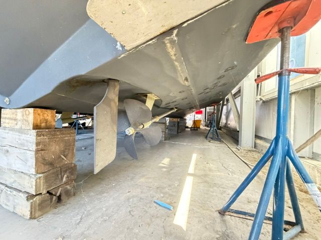 Underside of a yacht with propeller and supports in a dry dock.