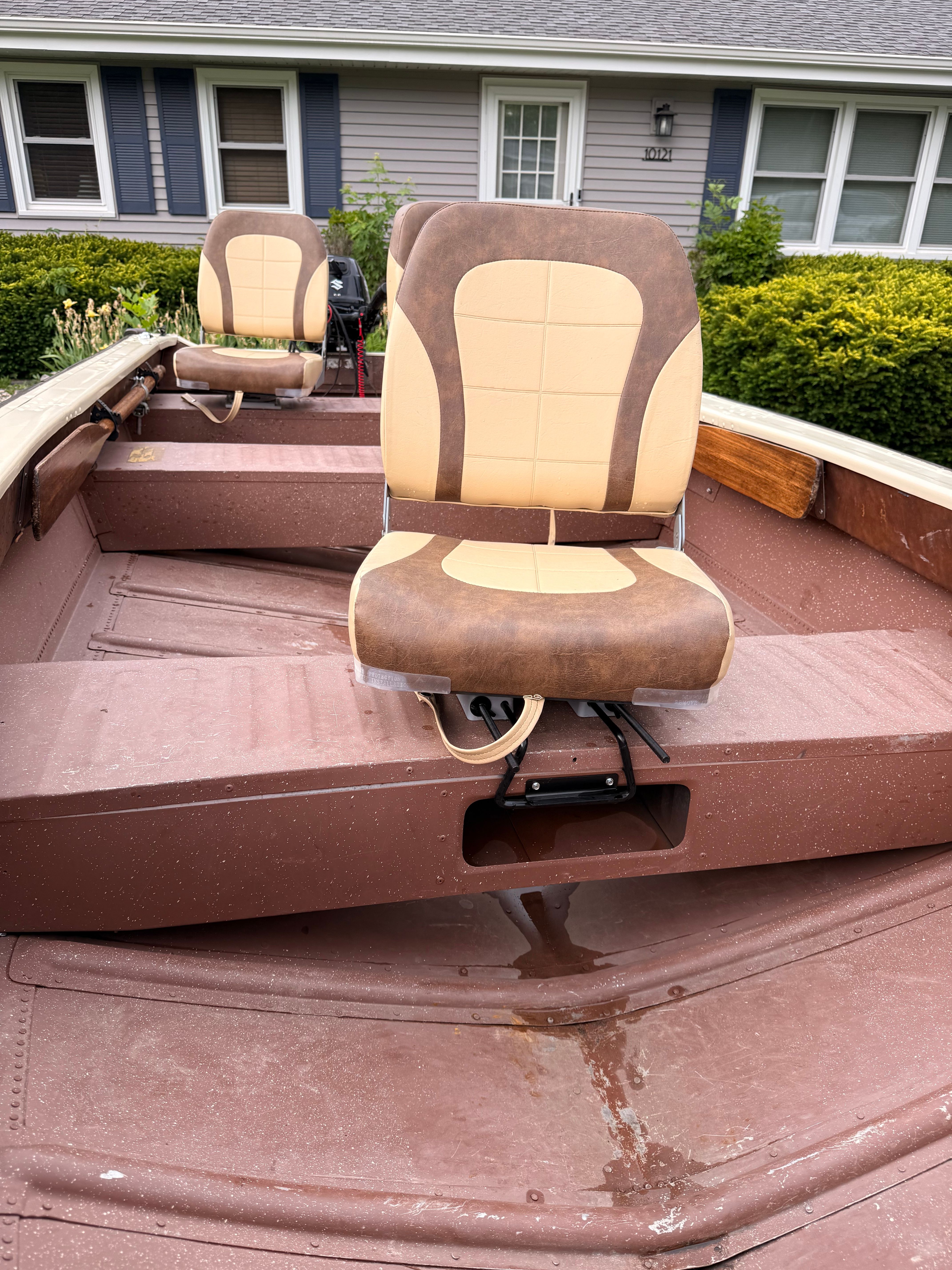 A 1985 Grumman 4.4 boat with two cushioned seats, situated on a lawn.