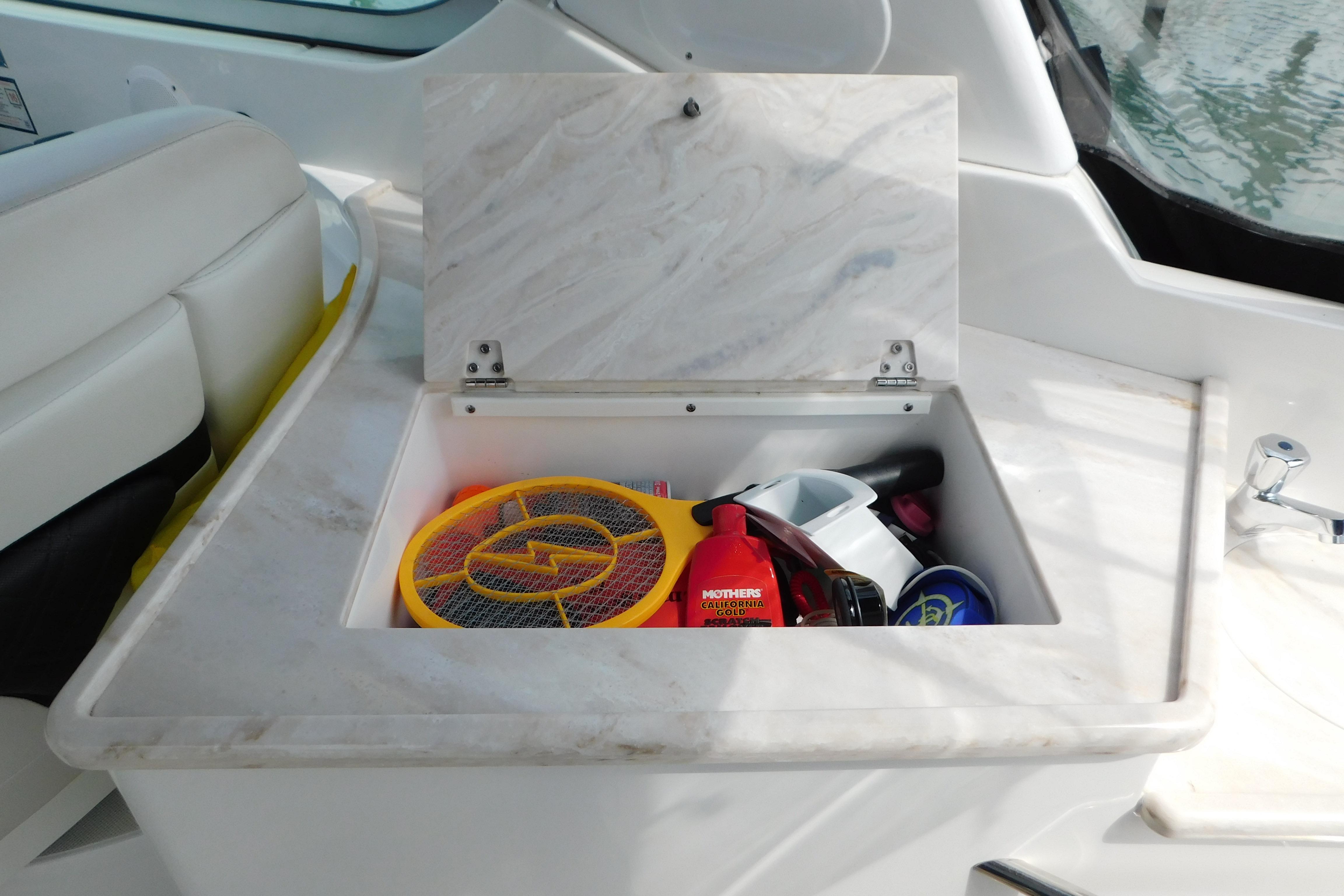 Open storage compartment on 2017 Rinker EX 320 boat with various items inside.