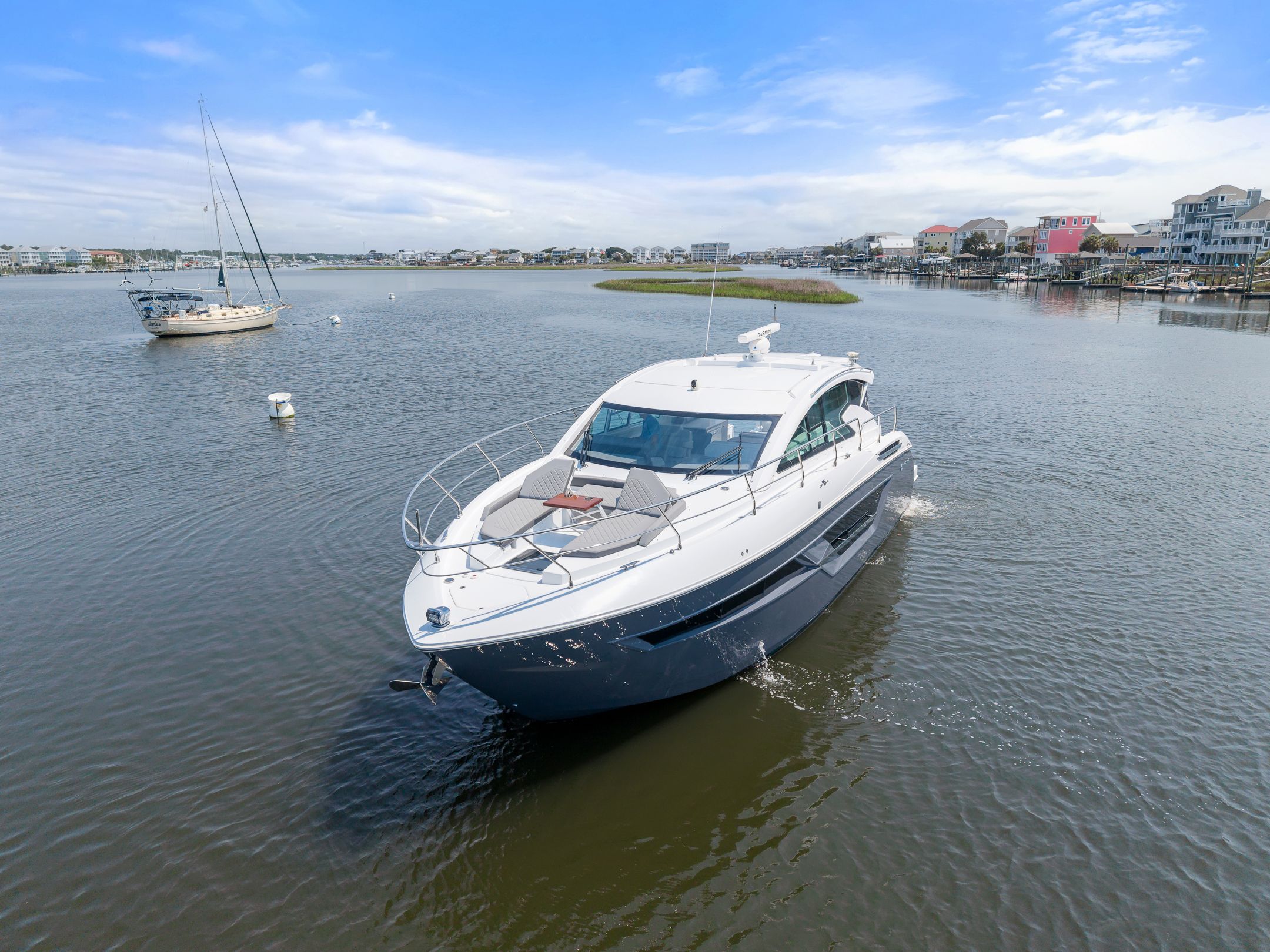 2023 Cruisers Yachts 46 Cantius on calm water near coastal town.