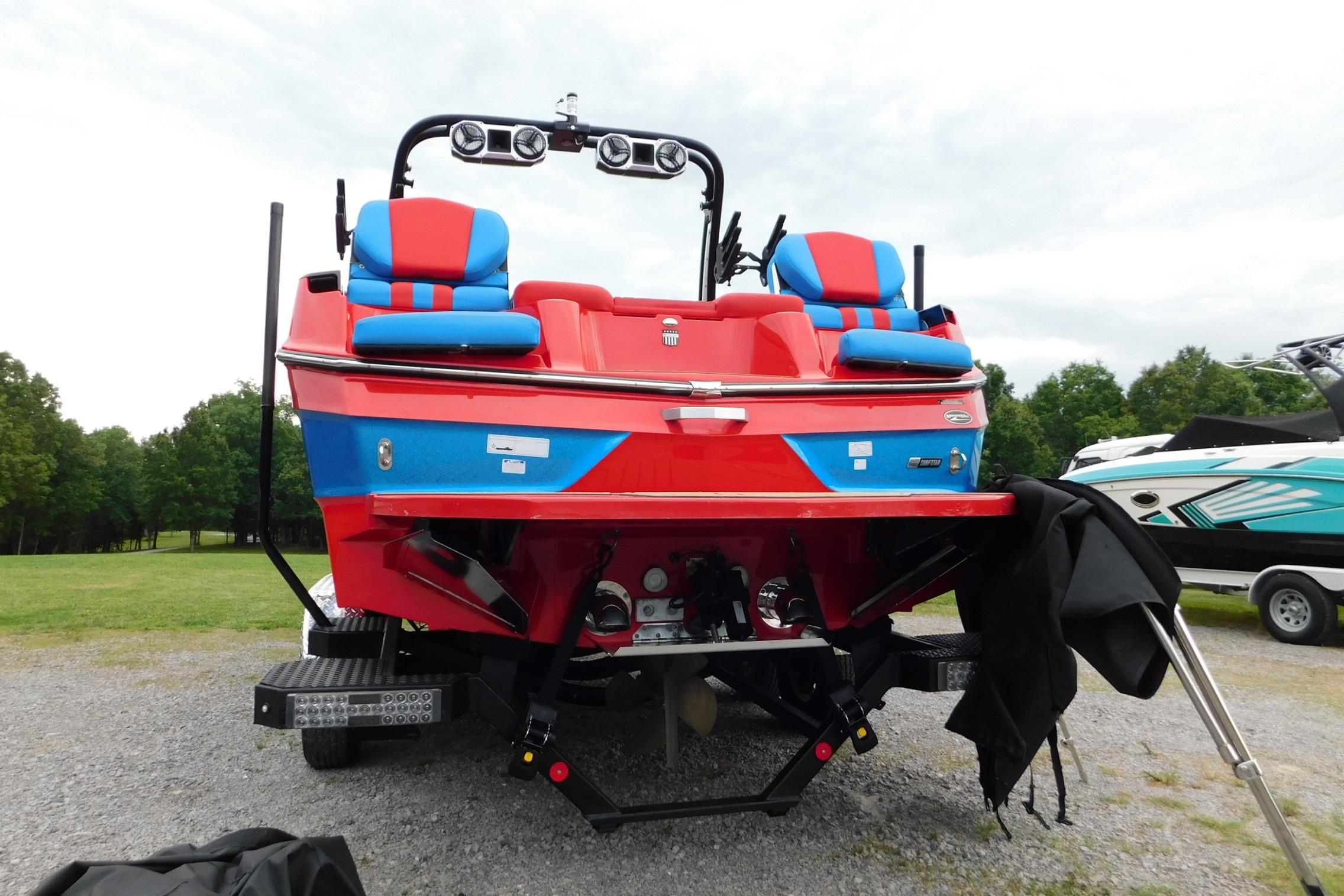 2022 MasterCraft NXT24 boat with vibrant red and blue design, parked on gravel.