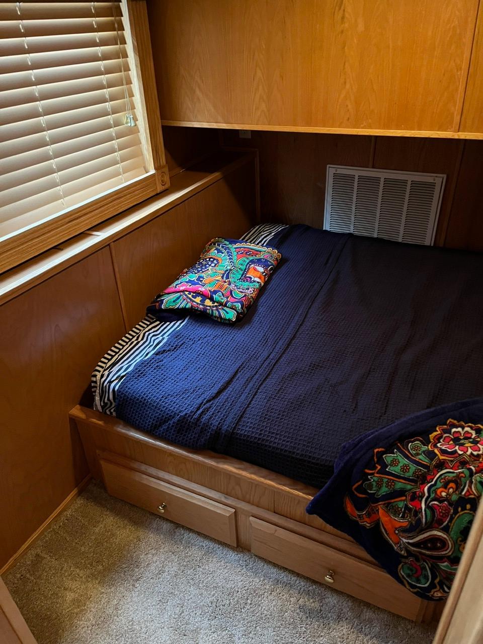 Cozy bedroom in a 2003 Lakeview houseboat with wooden interior and colorful bedding.