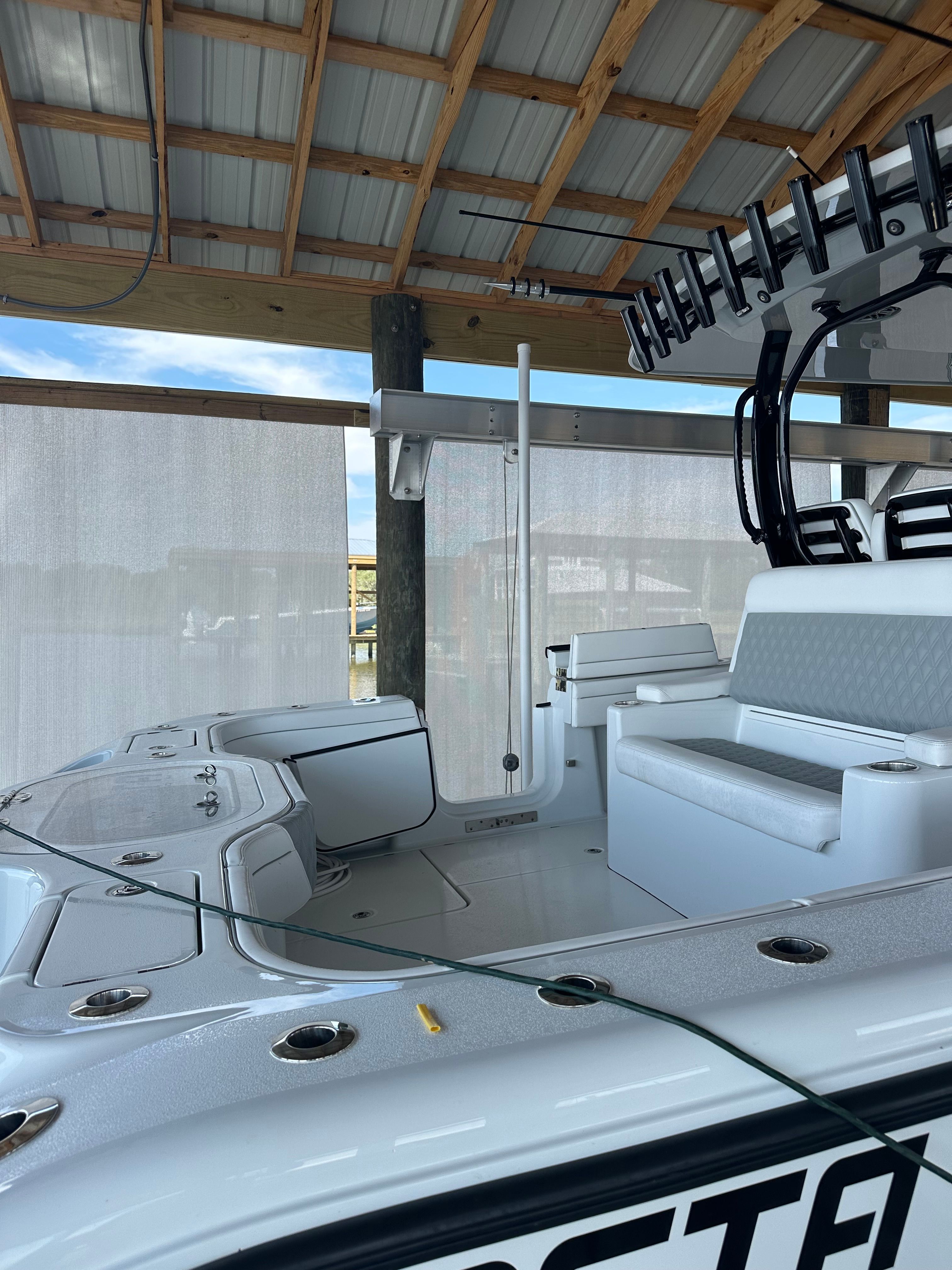 A modern boat with cushioned seating and rod holders under a covered dock.