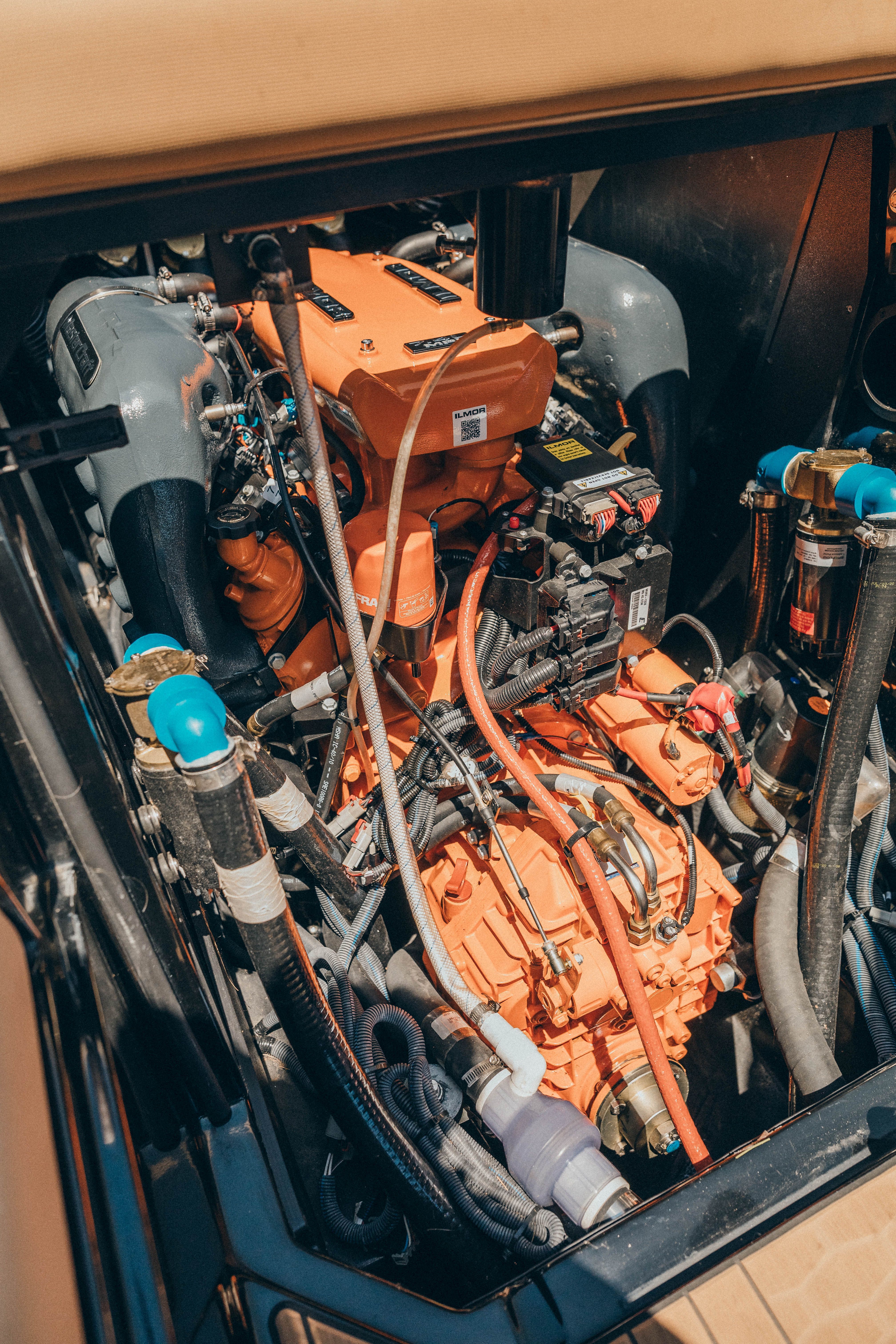 The engine compartment of a 2021 MasterCraft X26 features an orange engine with hoses and cables.