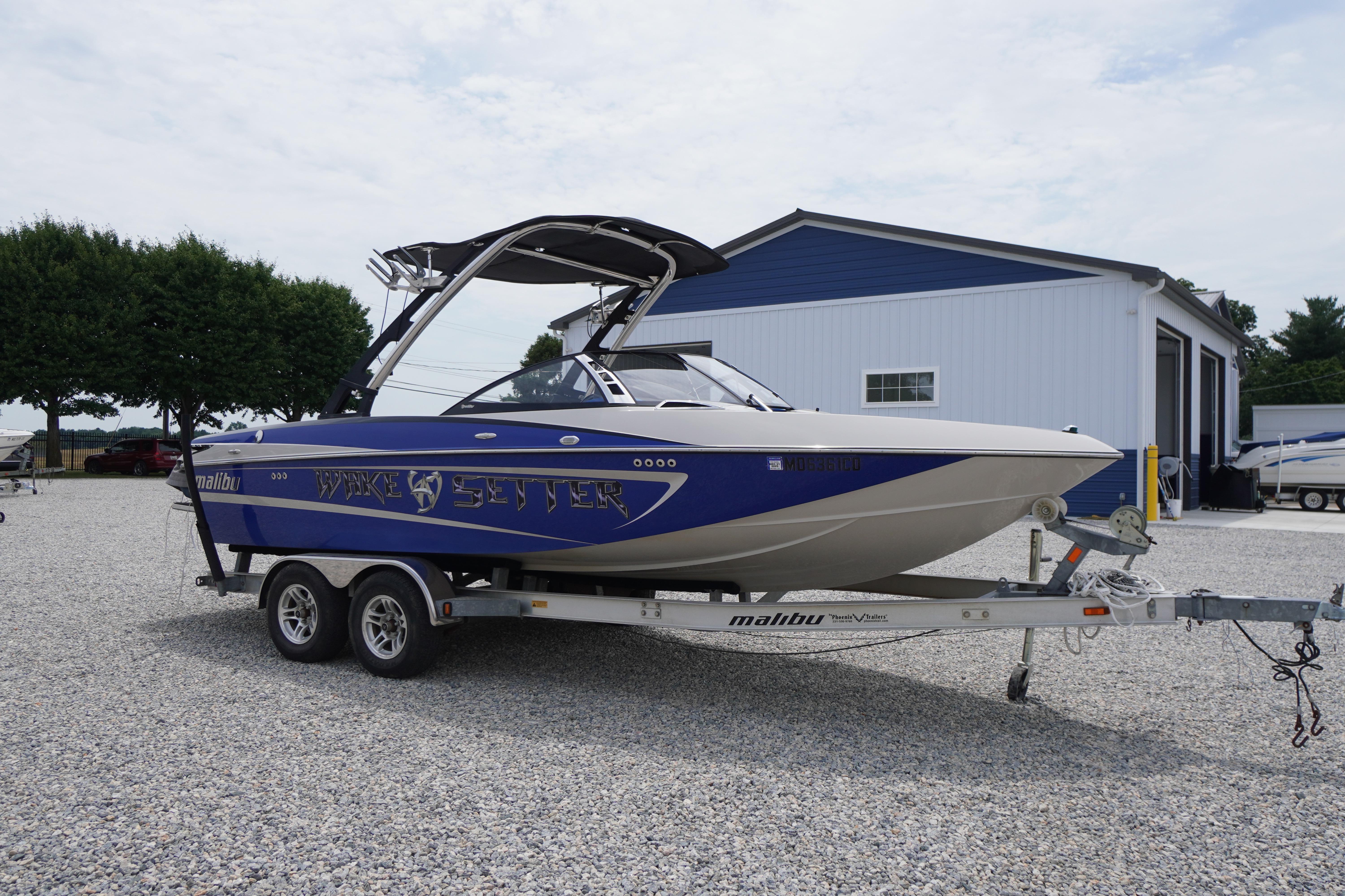 2011 Malibu Wakesetter 21 VLX boat on trailer, parked outside a blue building.