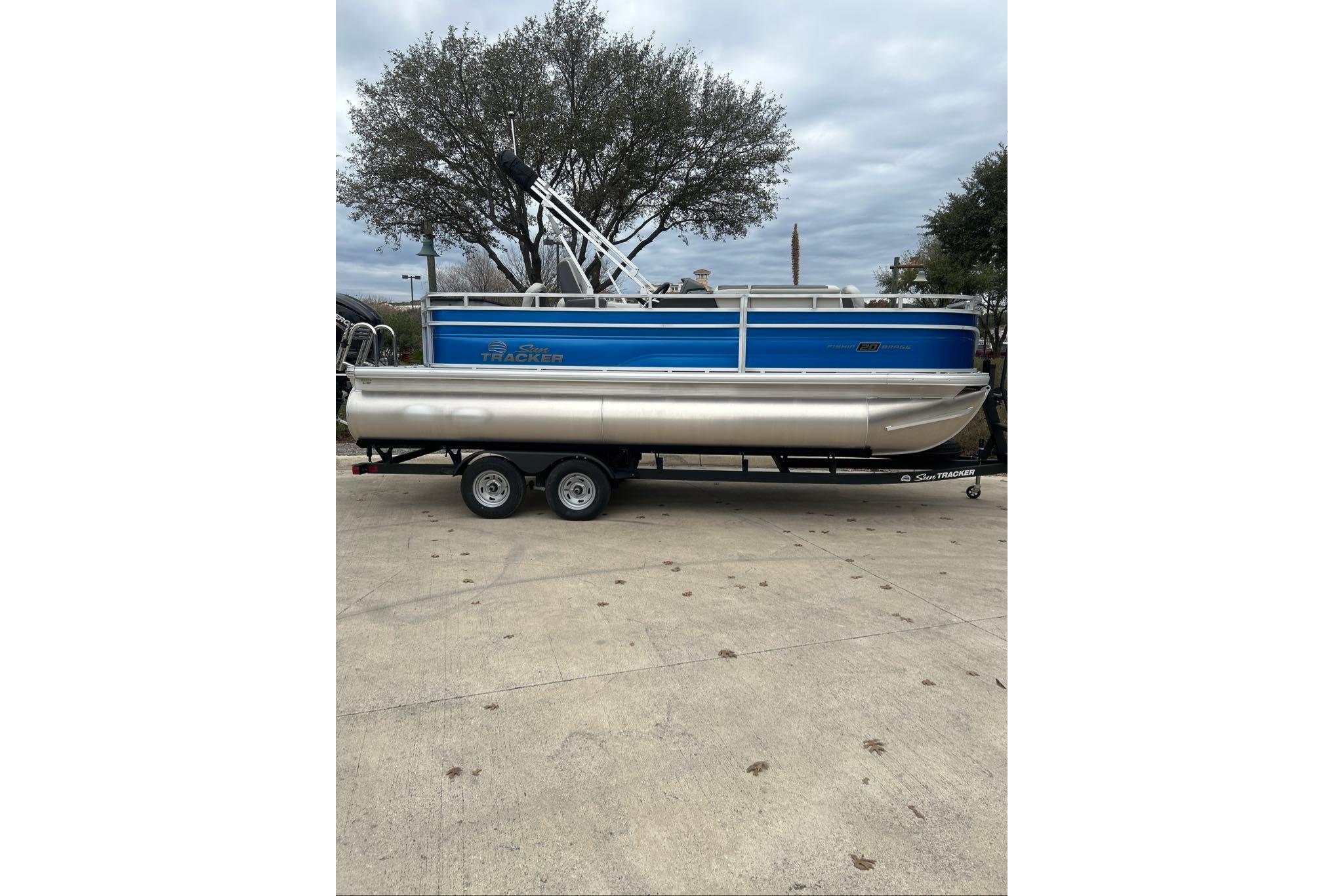 2026 Sun Tracker Fishin' Barge 20 DLX pontoon boat on trailer, parked outdoors.