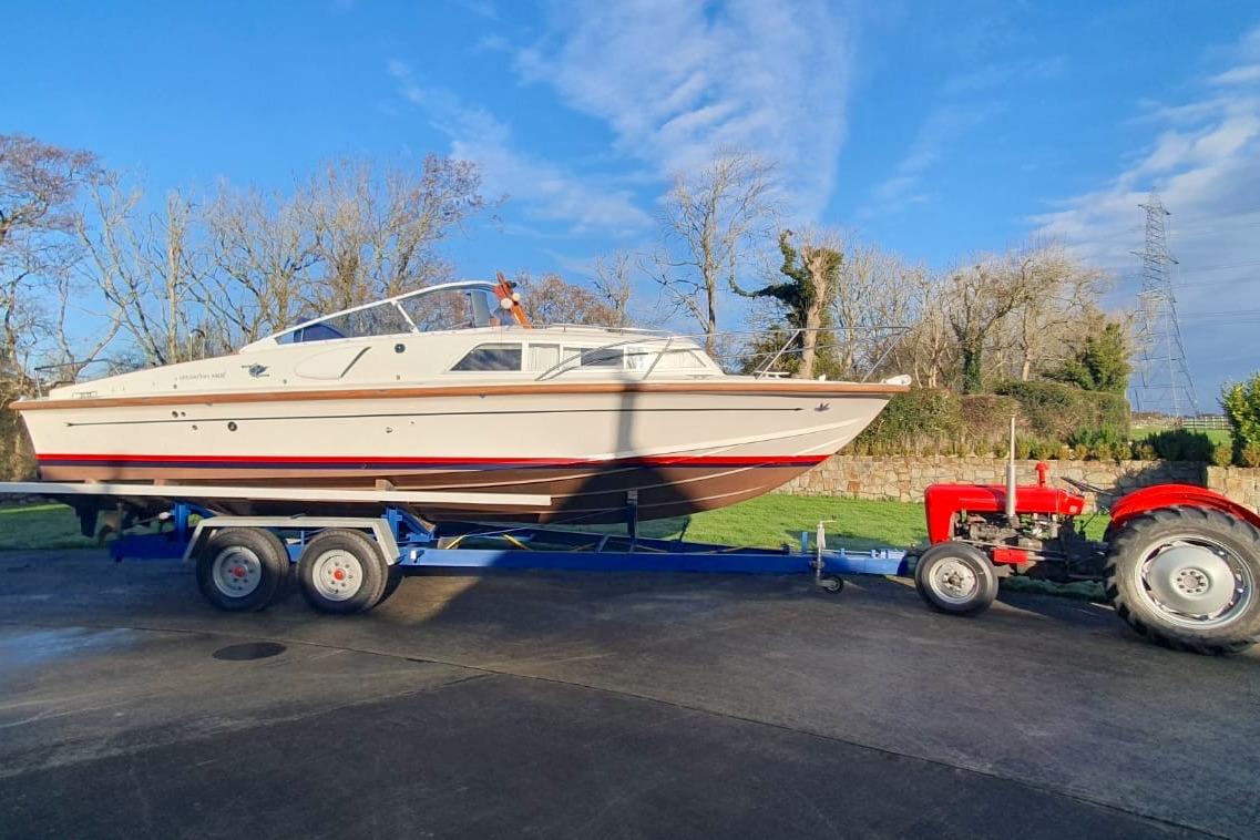 Fairey Spearfish MKIII 1989 boat on trailer, towed by a red tractor, outdoors.